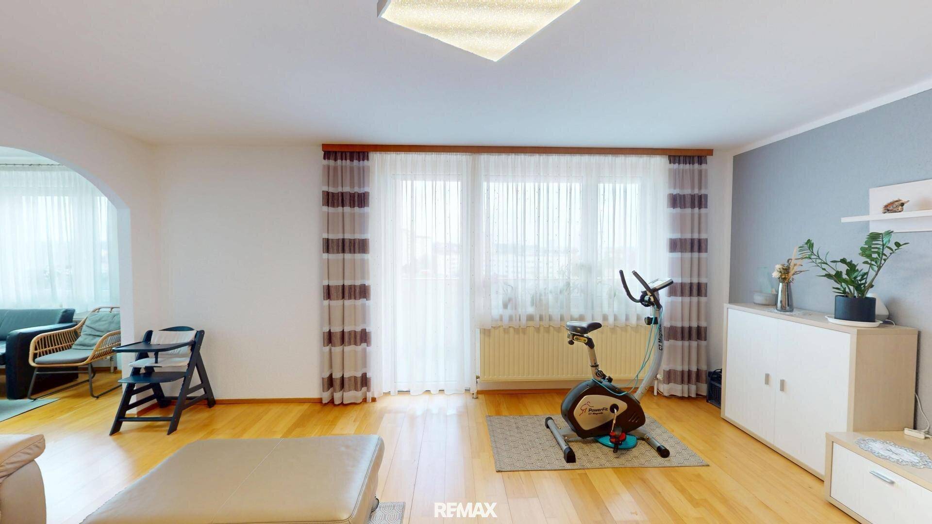 Helles Wohnzimmer mit Holzboden, großem Fenster und Fitnessgerät.