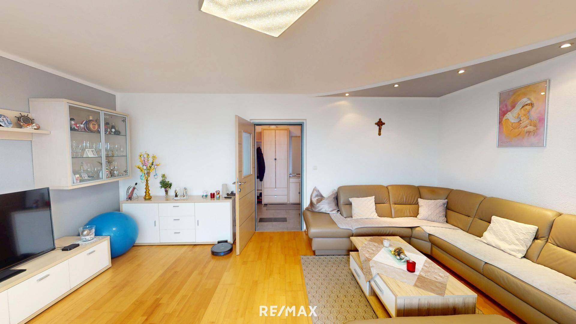 Wohnzimmer mit beigem Ecksofa, Couchtisch, TV-Möbel und Zugang zu einem weiteren Raum.