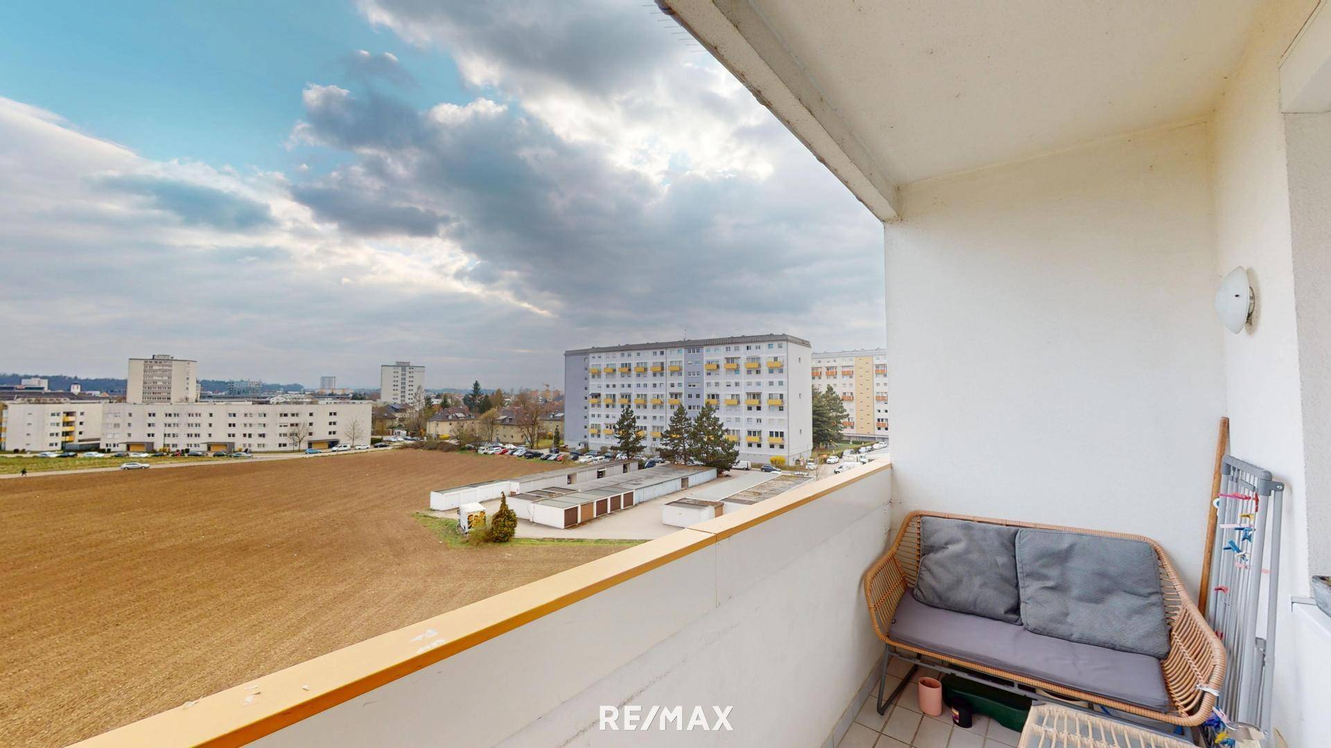 Balkon mit Sitzgelegenheit und weitem Blick über eine Grünfläche und Wohngebäude.