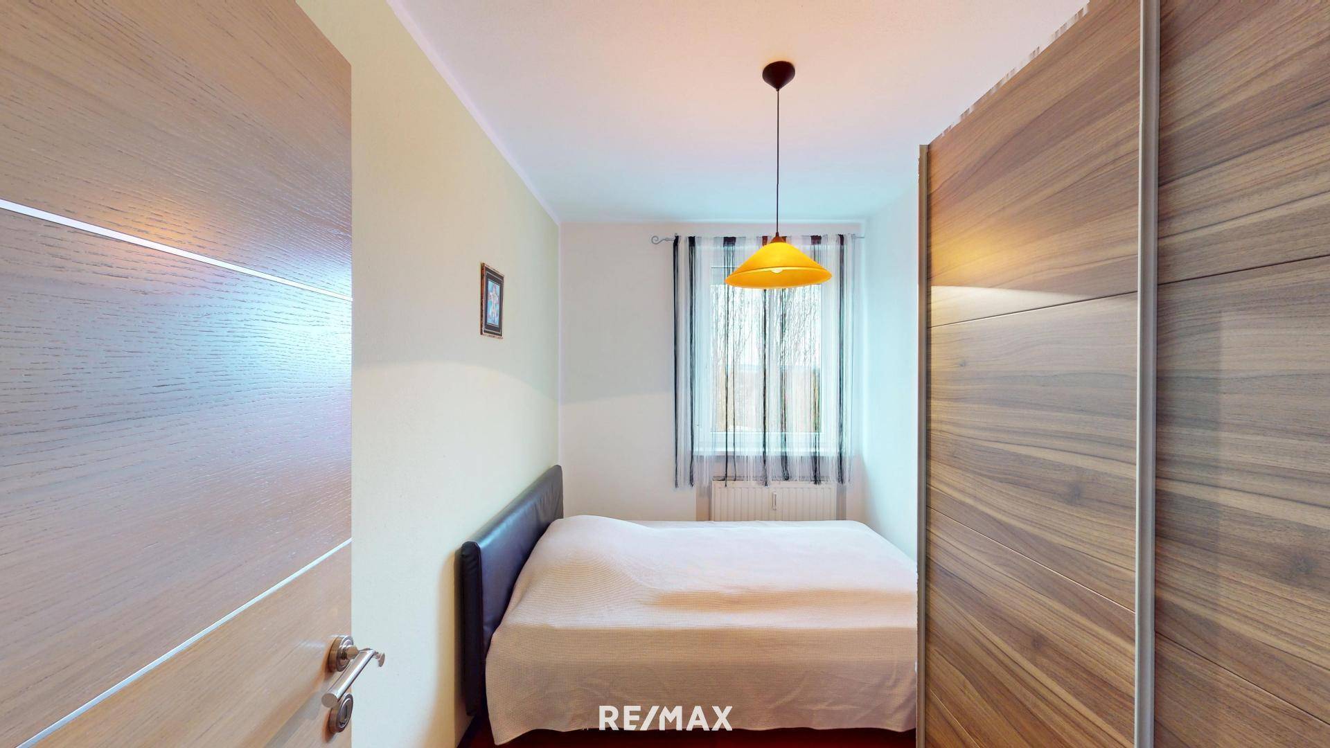 Schlafzimmer mit Doppelbett, großem Holzschrank und Fenster mit Blick nach draußen.