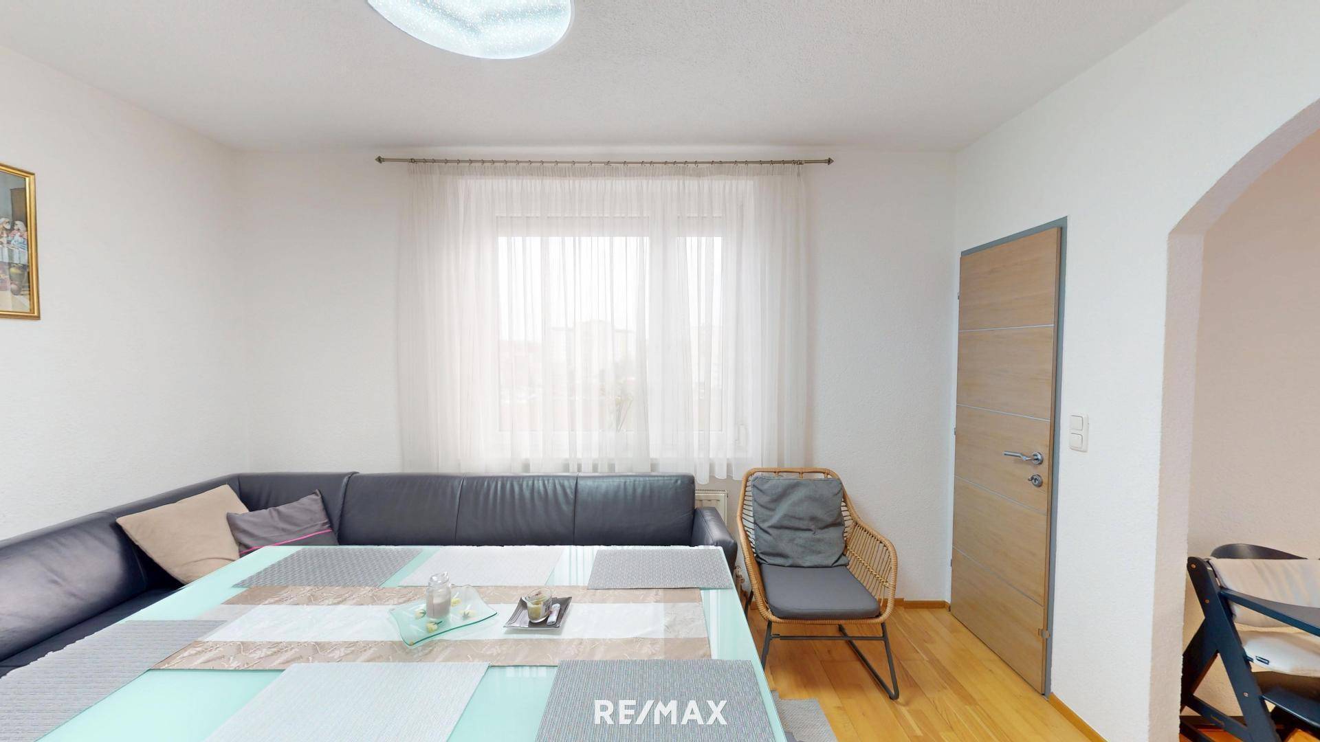 Essbereich mit dunklem Sofa, Esstisch und hellem Holzboden nahe einem Fenster.