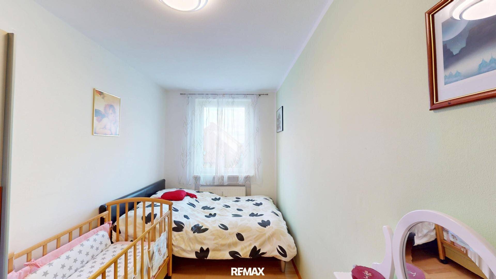 Schlafzimmer mit Doppelbett, Babybett und Fenster für natürliches Licht.