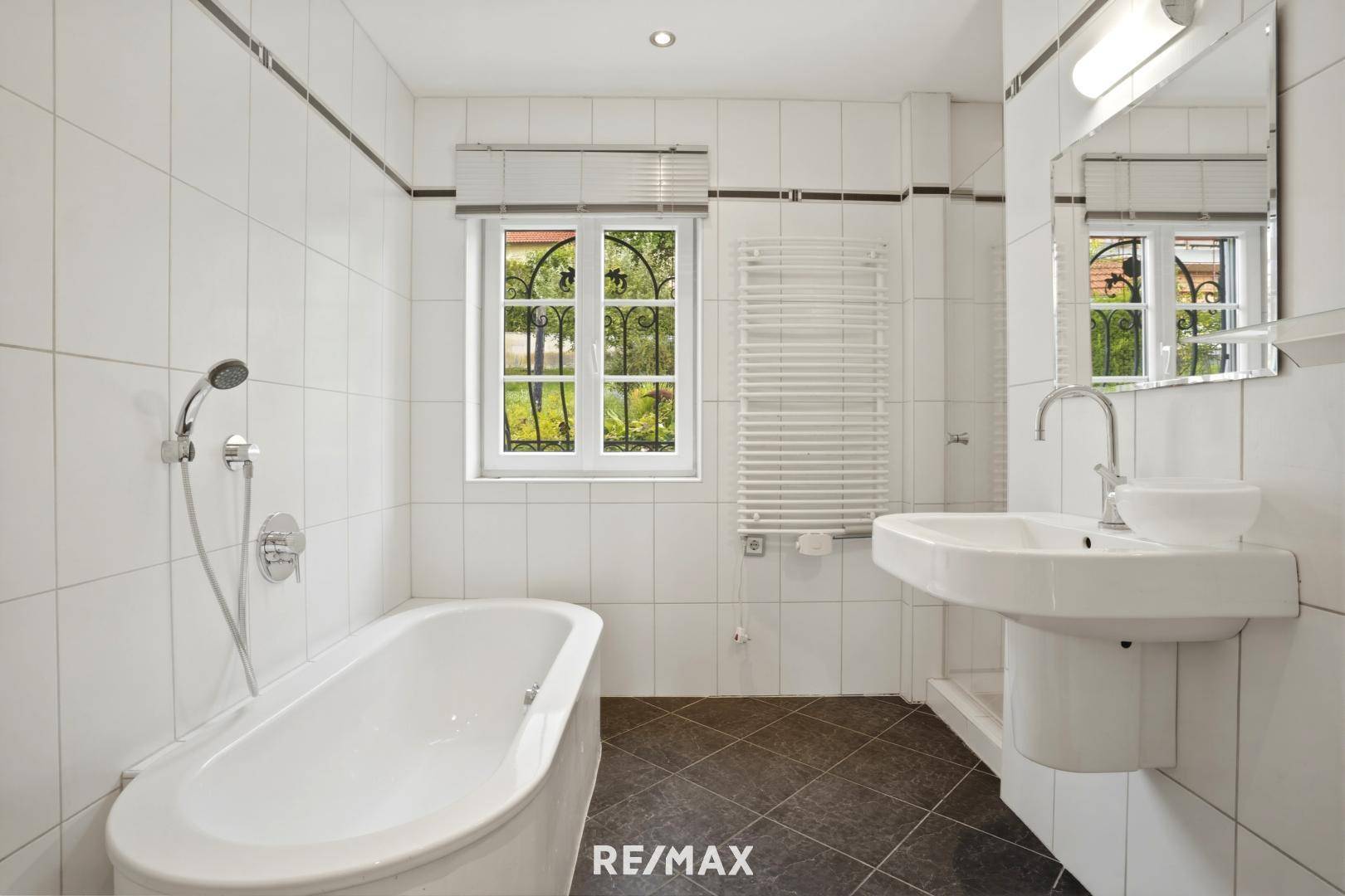 Gefliestes Badezimmer mit Badewanne, Waschbecken und Fenster für Tageslicht.