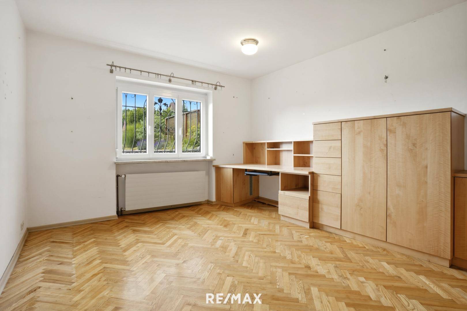 Kinderzimmer oder Büro mit Fischgrätparkett, Holzmöbeln und Fensterblick ins Grüne.