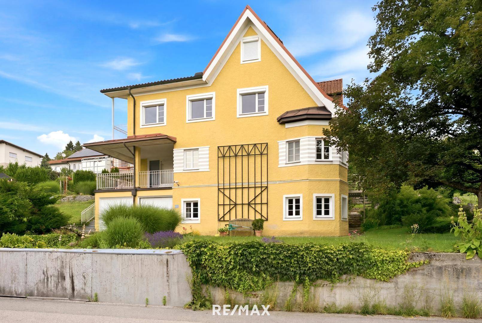 Ansicht des gelben Hauses mit Balkon und Gartenbereich von der Straße aus.