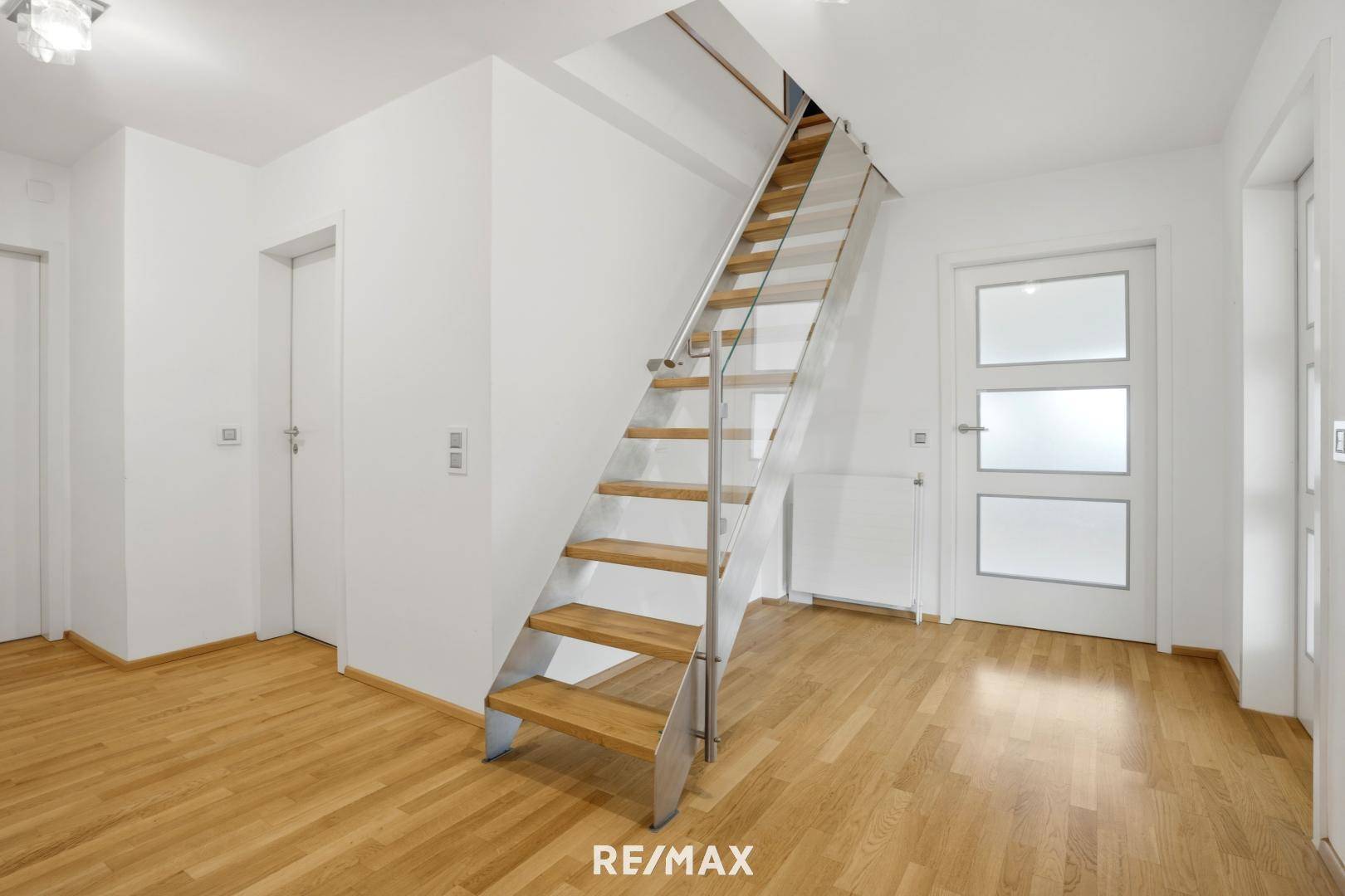 Heller Flur mit moderner Holztreppe und Glasgeländer, verbindet die Etagen.
