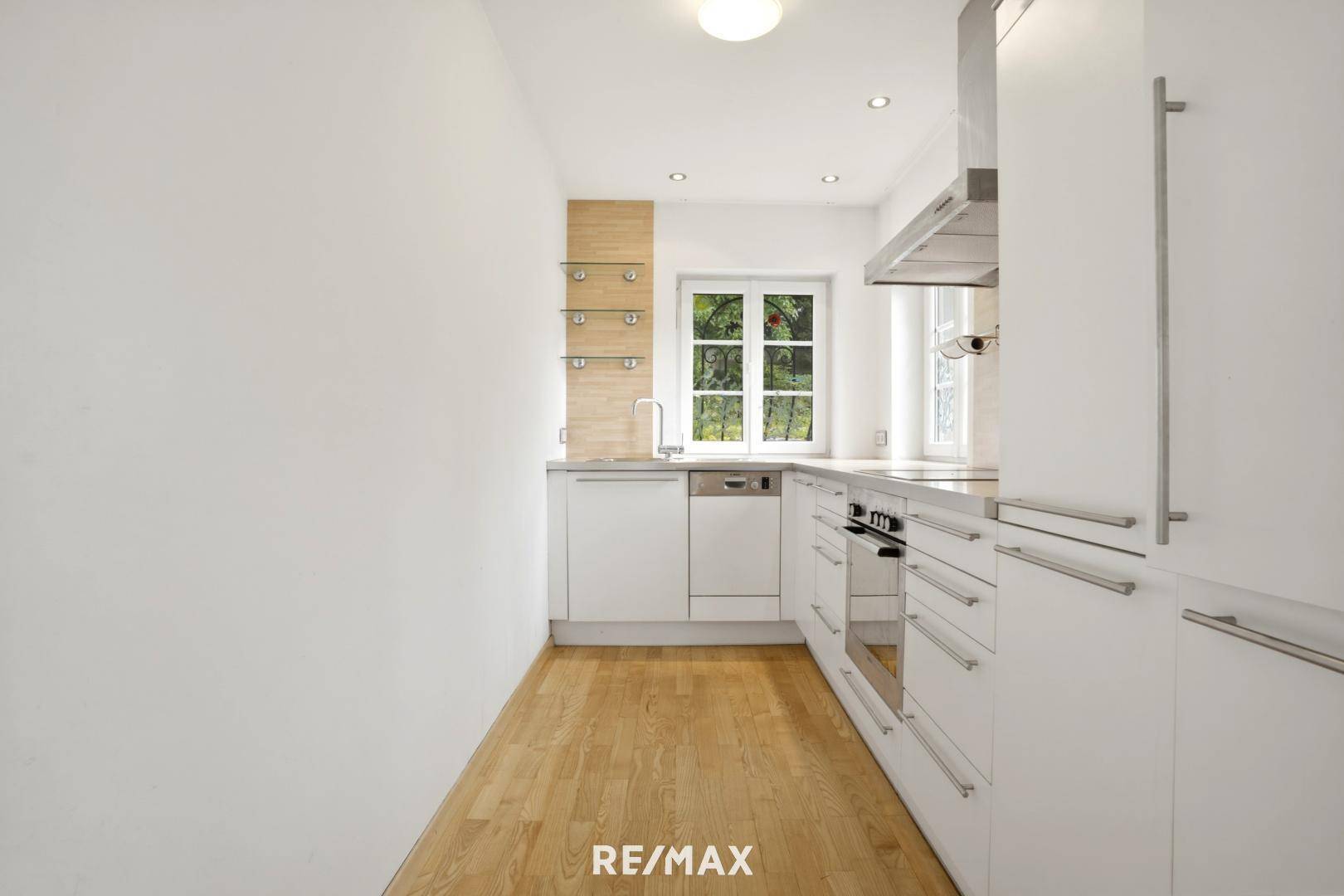 Moderne Einbauküche mit weißen Schränken, Holzdetails und Fenster mit Blick ins Grüne.