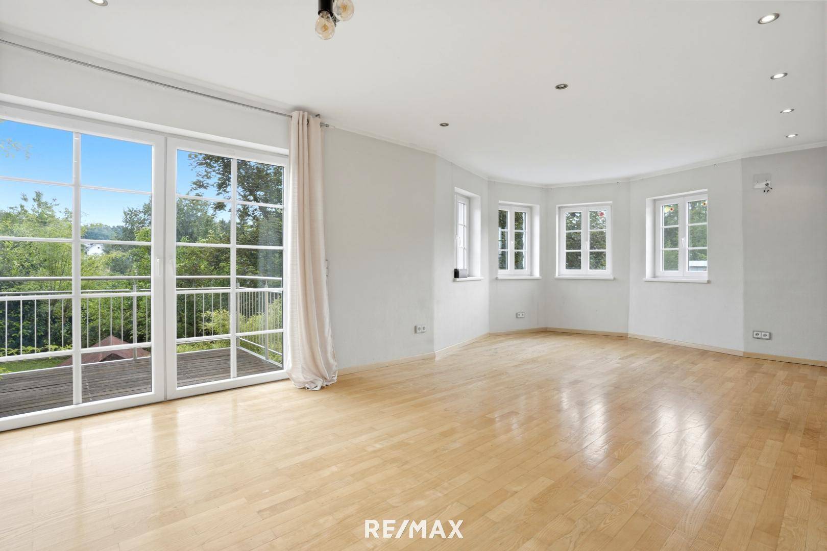 Helles Wohnzimmer mit großen Fenstern, Holzboden und Zugang zum Balkon.