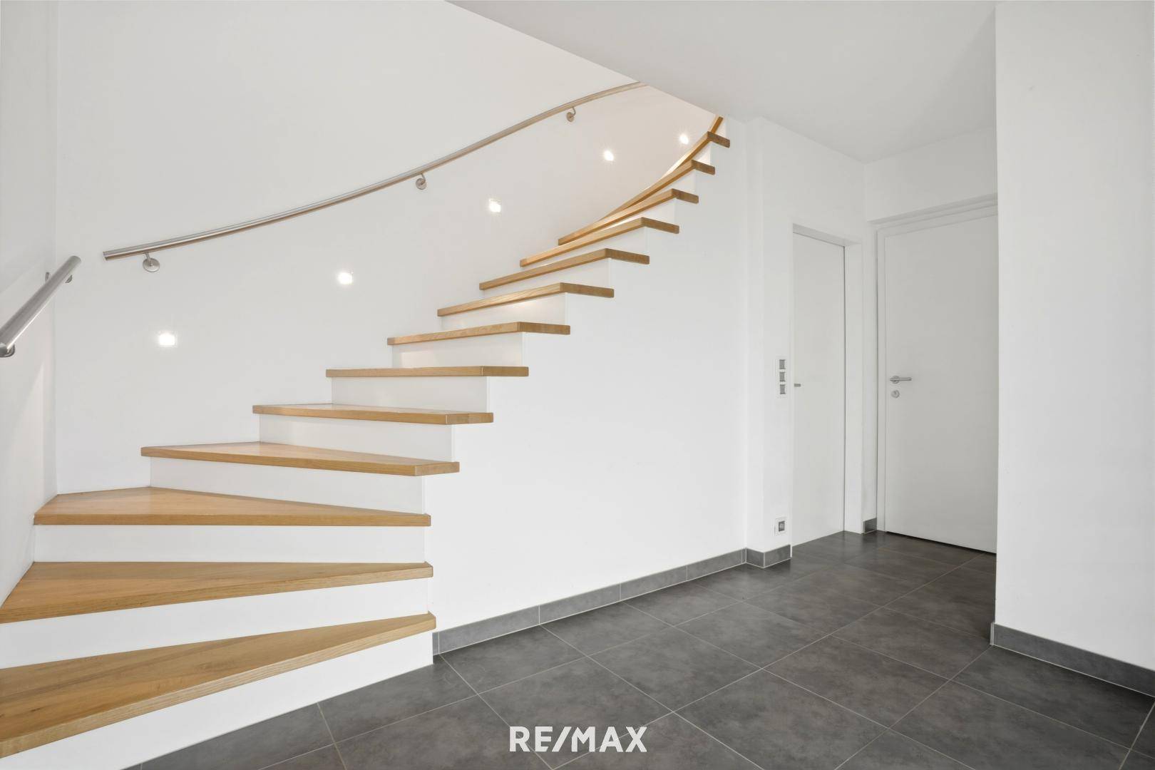 Moderner Eingangsbereich mit geschwungener Holztreppe und dunklen Fliesen.