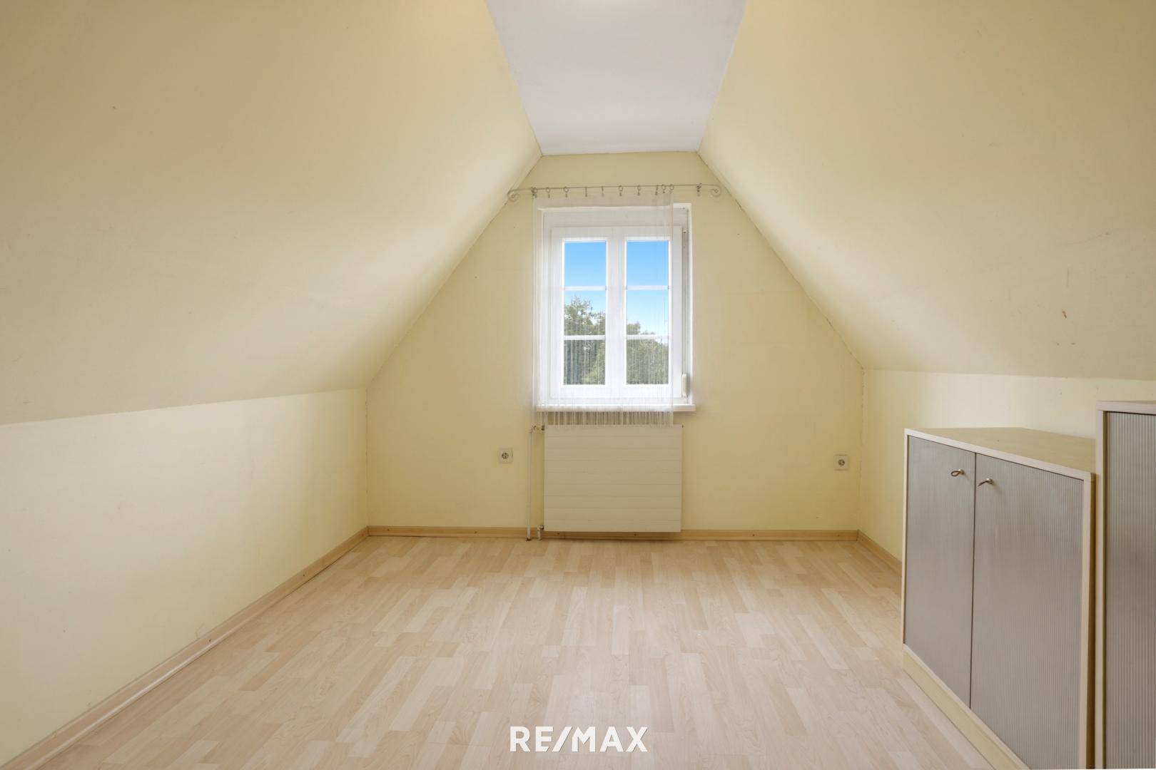 Dachgeschosszimmer mit schrägen Wänden, hellem Boden und Fenster für natürliches Licht.