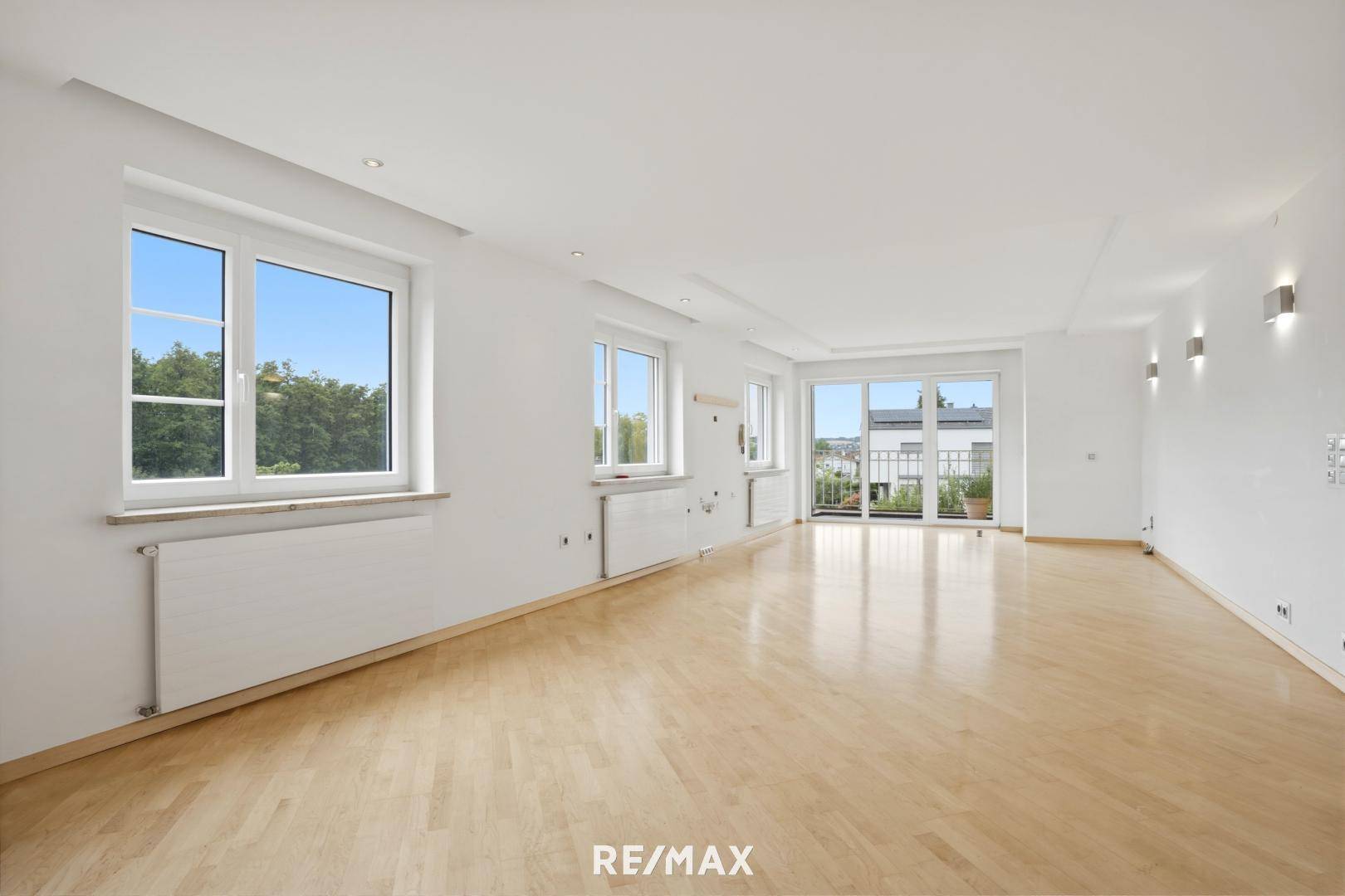 Großzügiges Wohnzimmer mit hellem Parkettboden und Zugang zu einem weiteren Balkon.