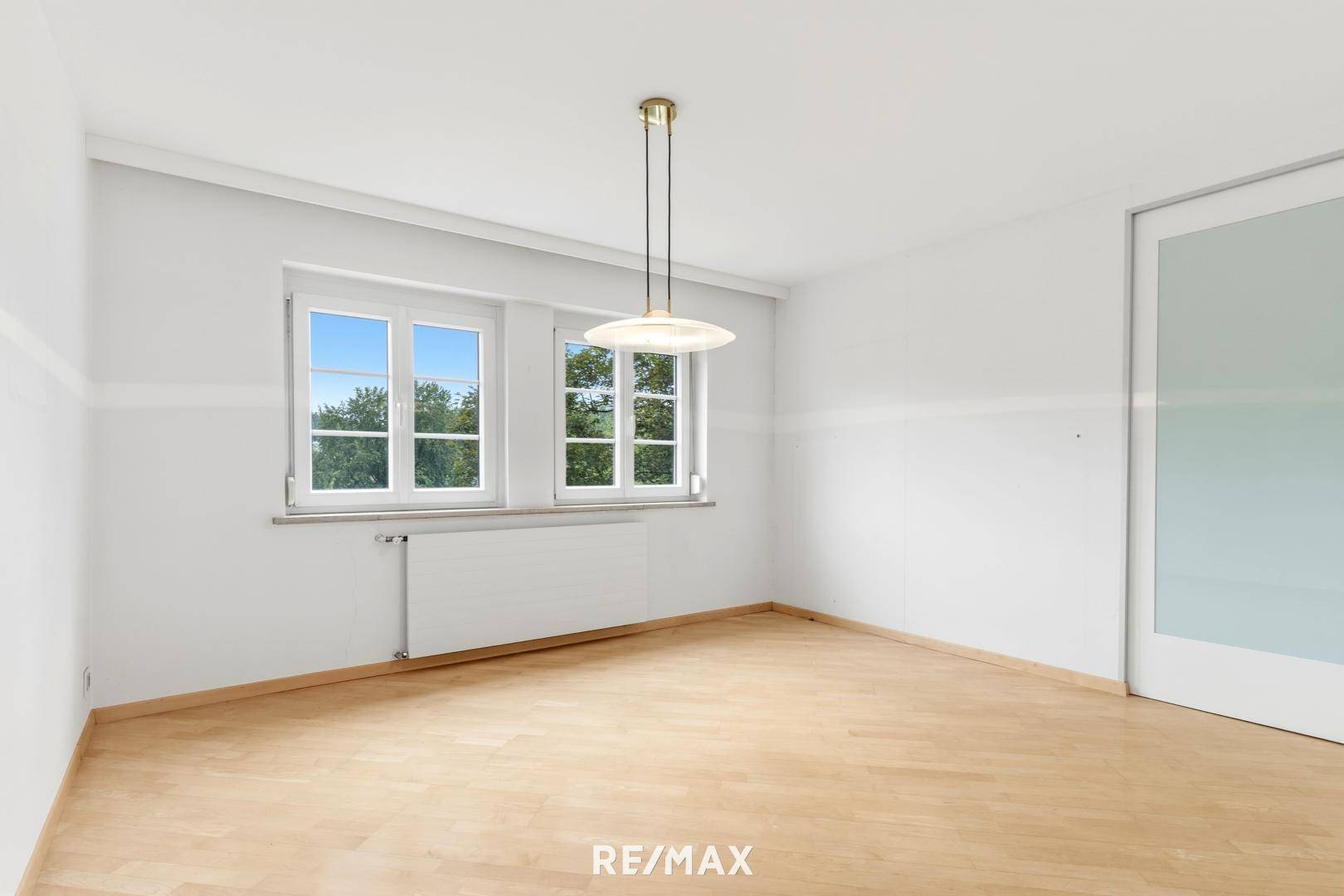 Helles Zimmer mit Holzboden und zwei Fenstern, geeignet als Schlaf- oder Gästezimmer.