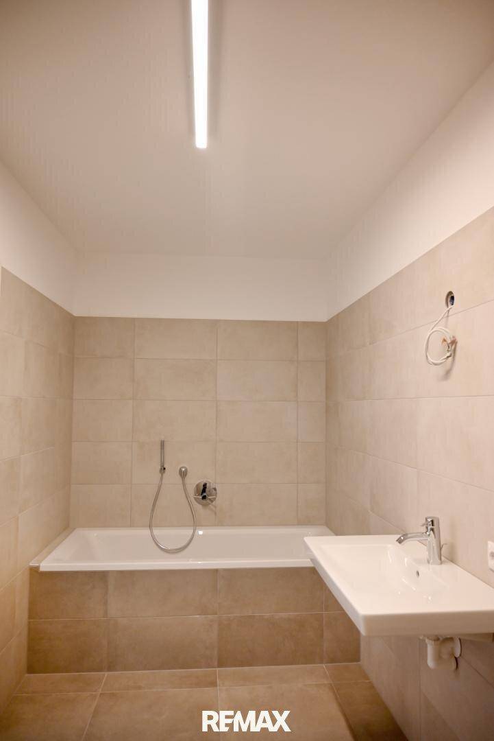 Modernes Badezimmer mit beigefarbenen Fliesen, Badewanne und Waschbecken.