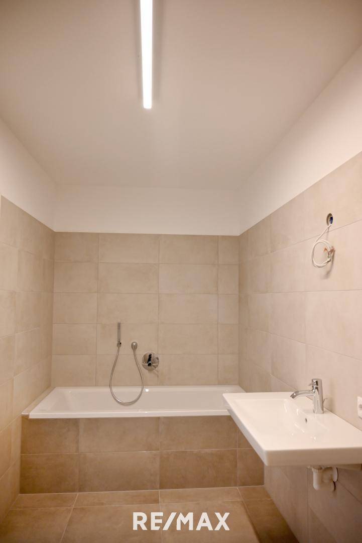 Modernes Badezimmer mit Badewanne, Waschbecken und beigefarbenen Fliesen.
