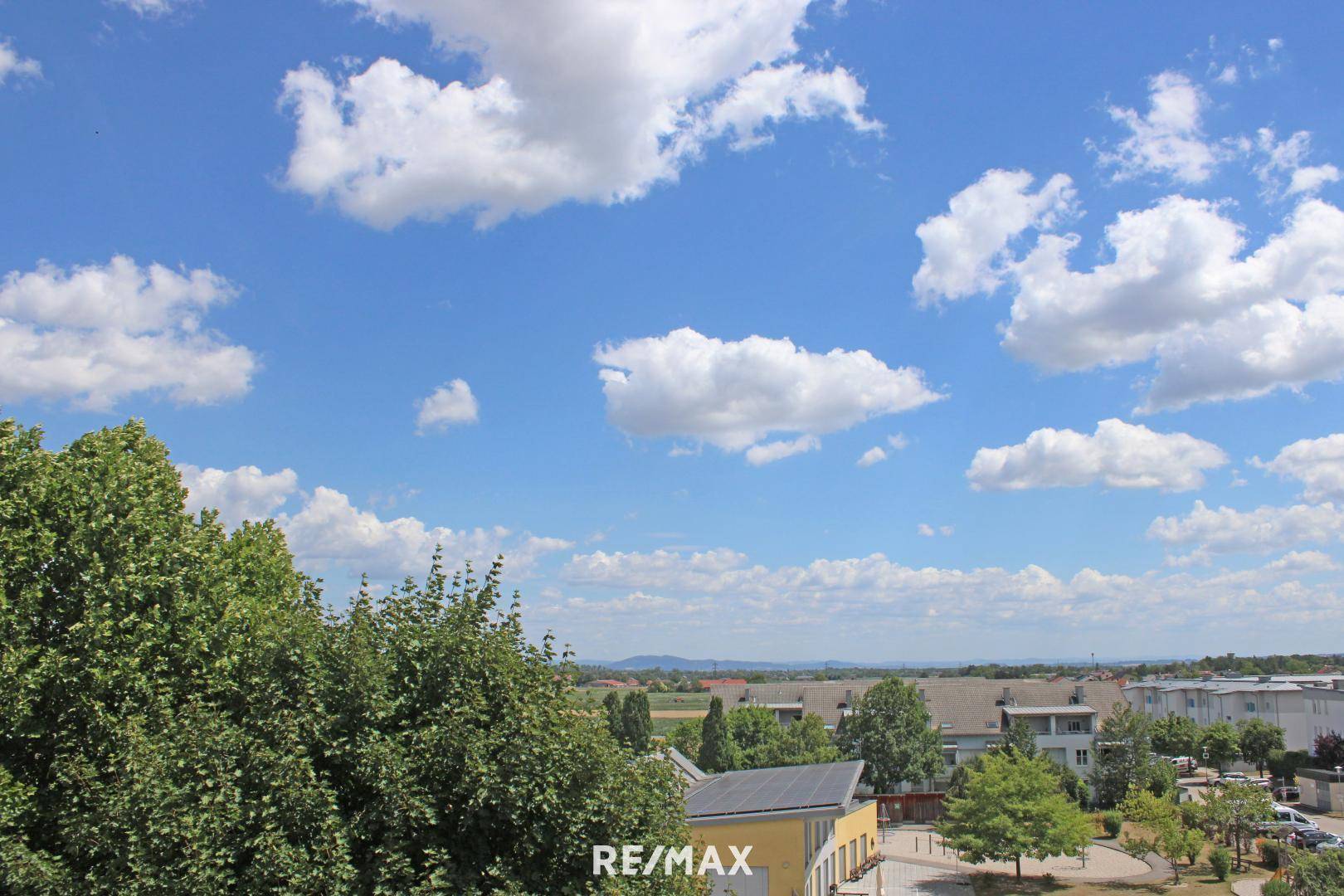 Panoramablick über eine grüne Wohngegend mit vielen Bäumen und weitem Horizont unter blauem Himmel.