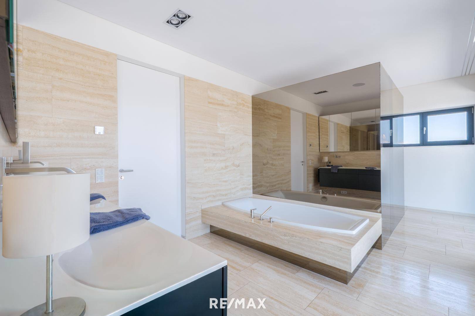 Elegantes Badezimmer mit integrierter Badewanne, doppelten Waschbecken und beigefarbenen Fliesen.