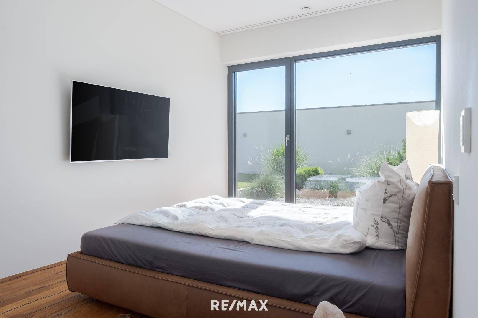 Modernes Schlafzimmer mit großem Bett, Holzboden und bodentiefen Fenstern mit Blick ins Grüne.