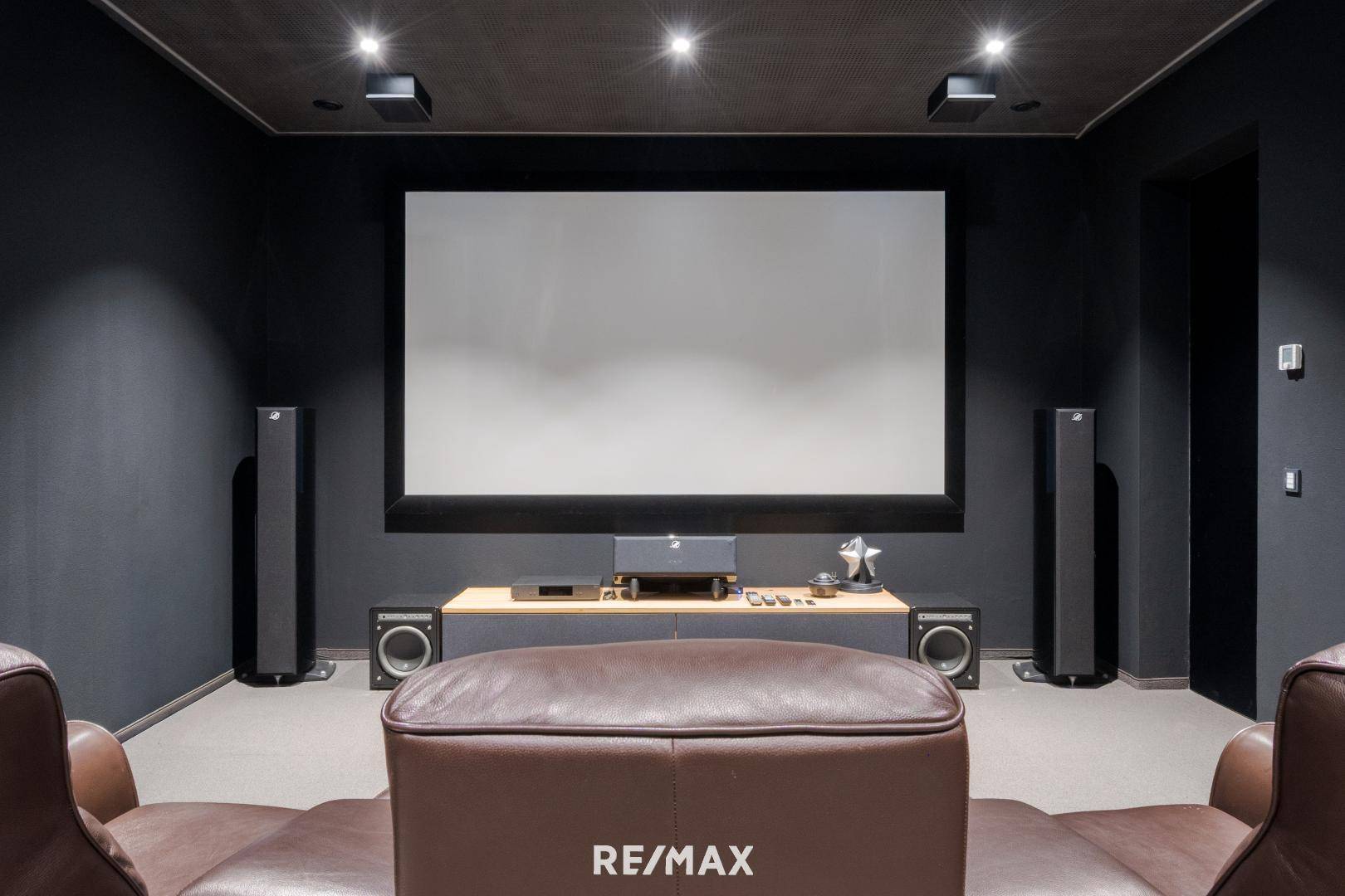 Exklusiver Heimkinoraum mit großer Leinwand, bequemen Ledersesseln und dunkler, schallgedämmter Ausstattung.