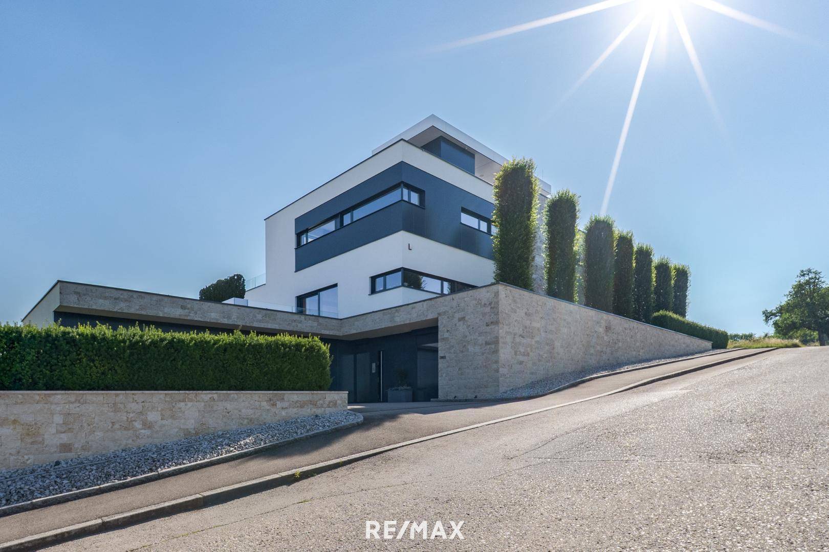 Moderne Architektur der Villa von der Zufahrt aus gesehen, umgeben von gepflegten Hecken und Steinmauern.