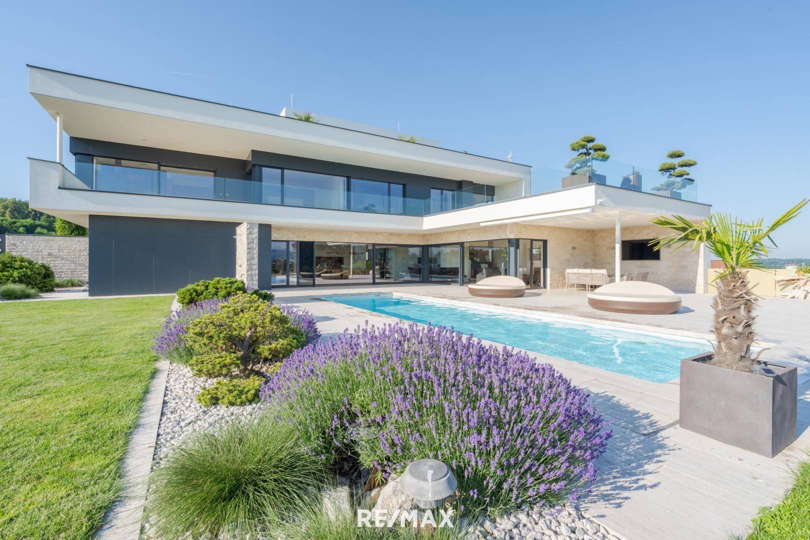 Gepflegter Gartenbereich mit blühendem Lavendel, Steinen und einem modernen Pool vor der Villa.