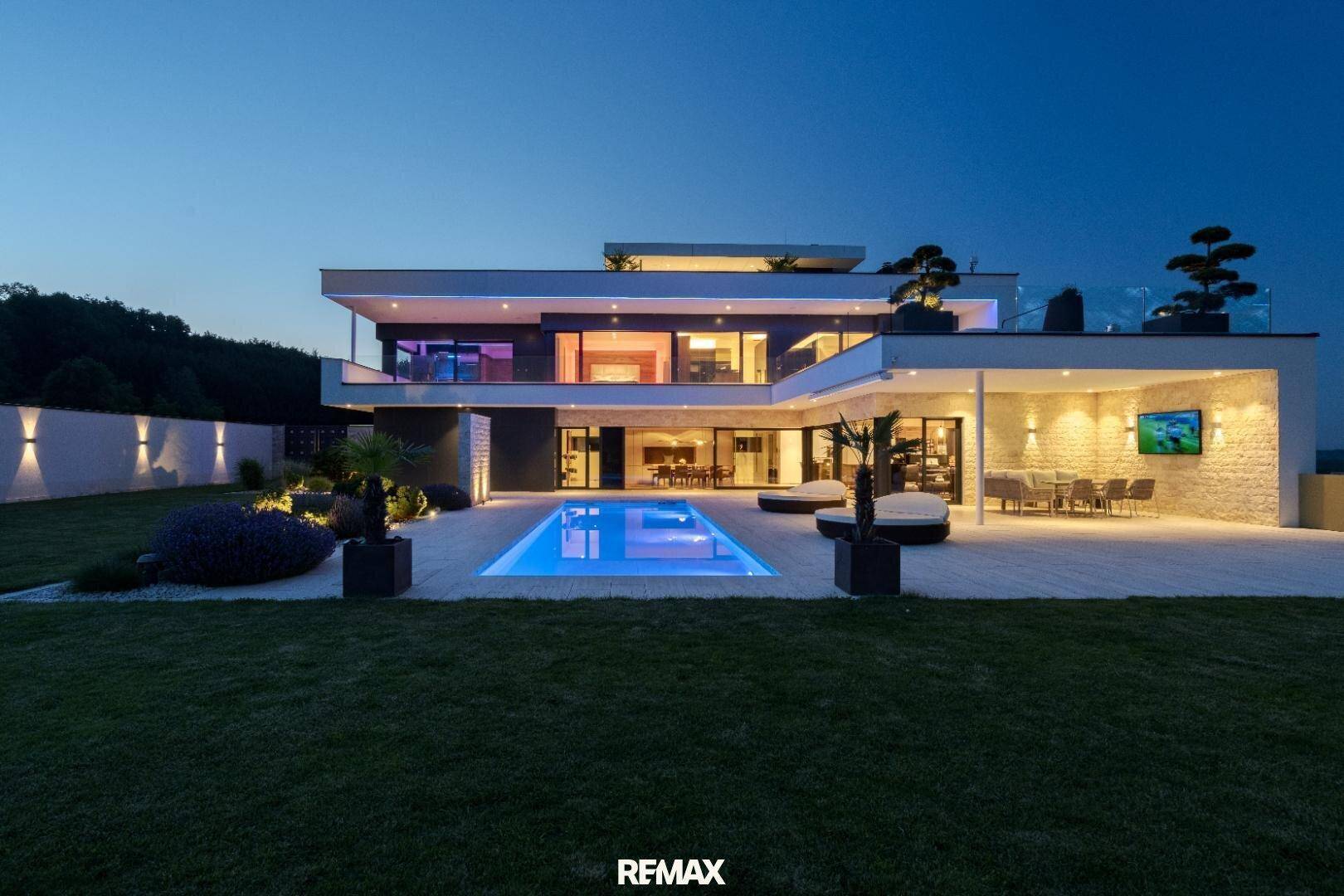 Moderne Luxusvilla bei Nacht mit beleuchtetem Pool, Garten und großzügigen Außenbereichen.