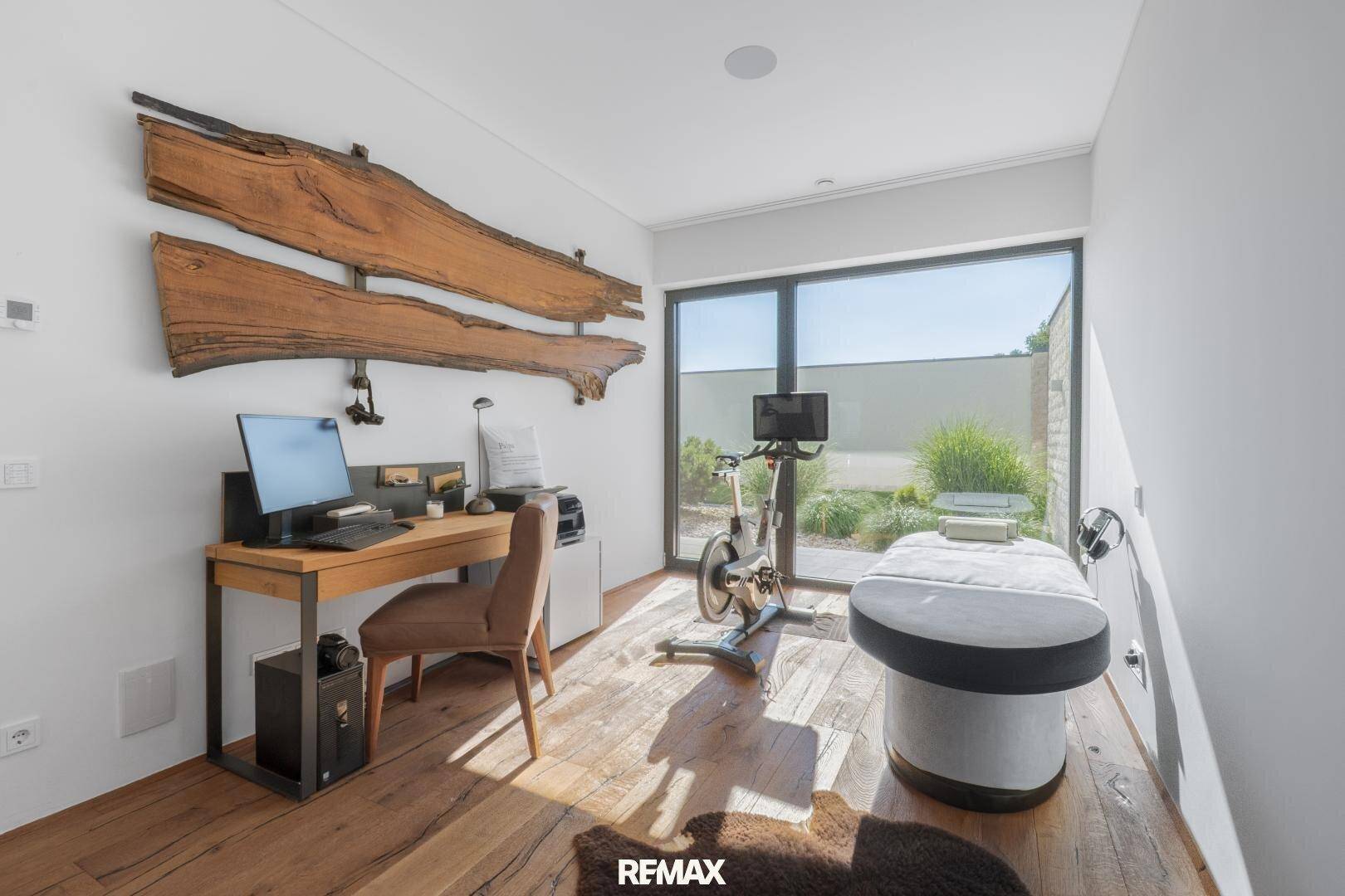 Helles Arbeitszimmer mit Holzboden, großem Fenster und einem Ergometer für sportliche Aktivitäten.