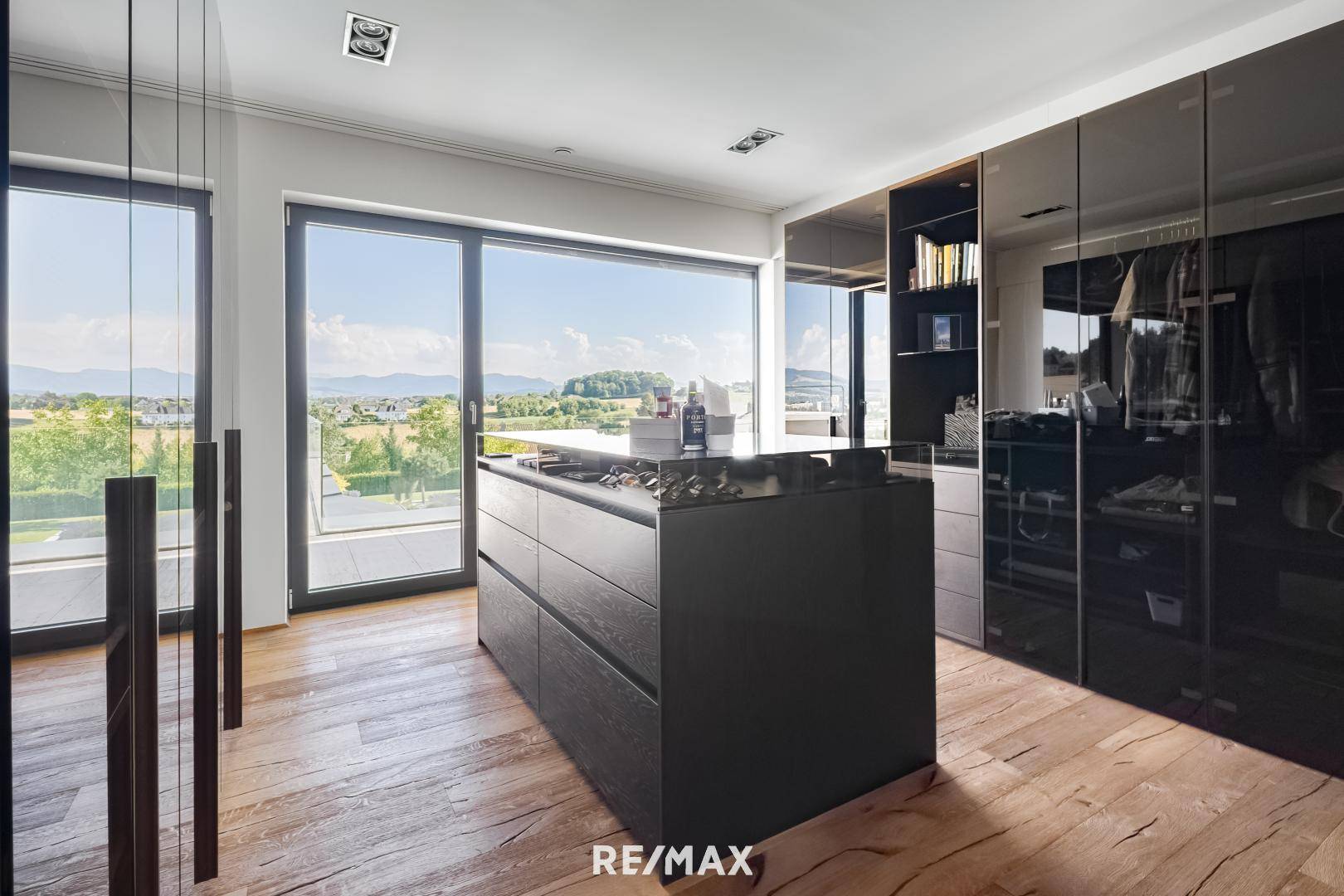 Geräumiger begehbarer Kleiderschrank mit dunklen Einbauschränken und großem Fenster mit Panoramablick.