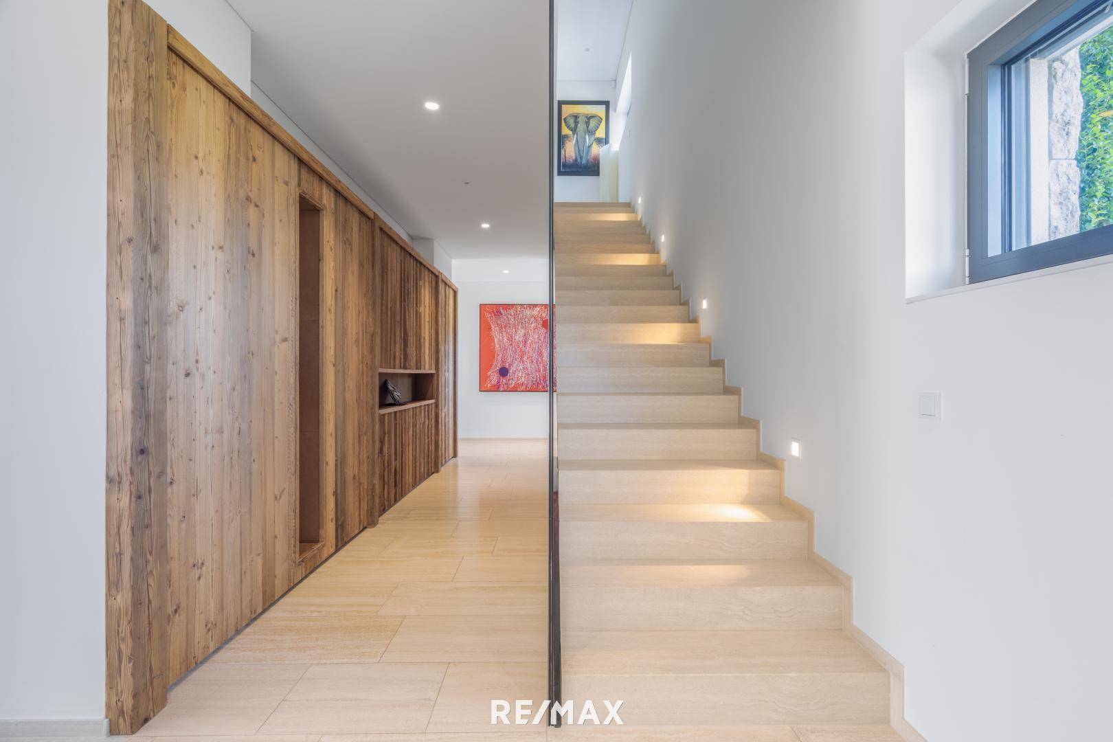 Heller Flur mit Holzverkleidung, moderner Treppe und indirekter Beleuchtung, die zum Obergeschoss führt.