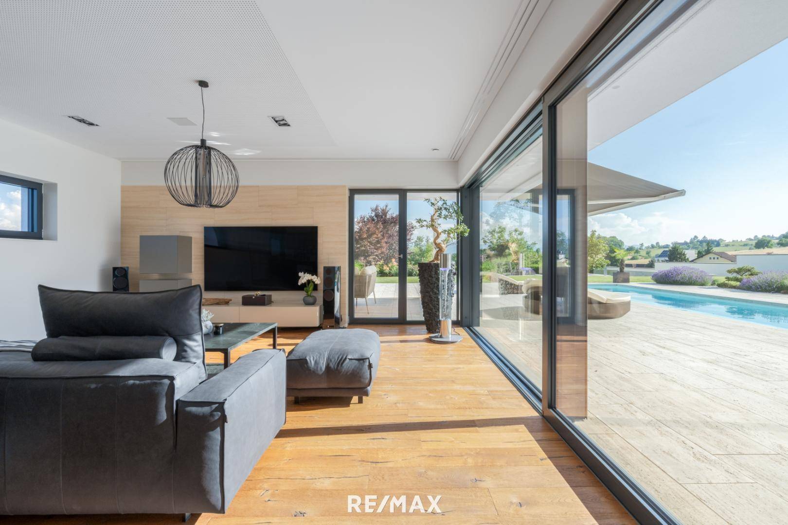 Geräumiges Wohnzimmer mit Holzboden, bequemer Couch und großen Schiebetüren zum Poolbereich.