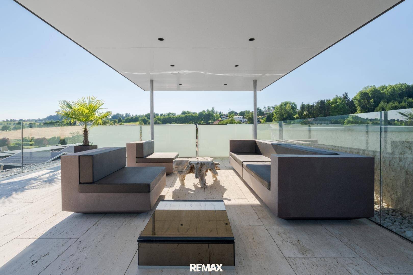 Überdachte Terrasse mit modernen Outdoor-Möbeln und weitem Blick in die grüne Landschaft.