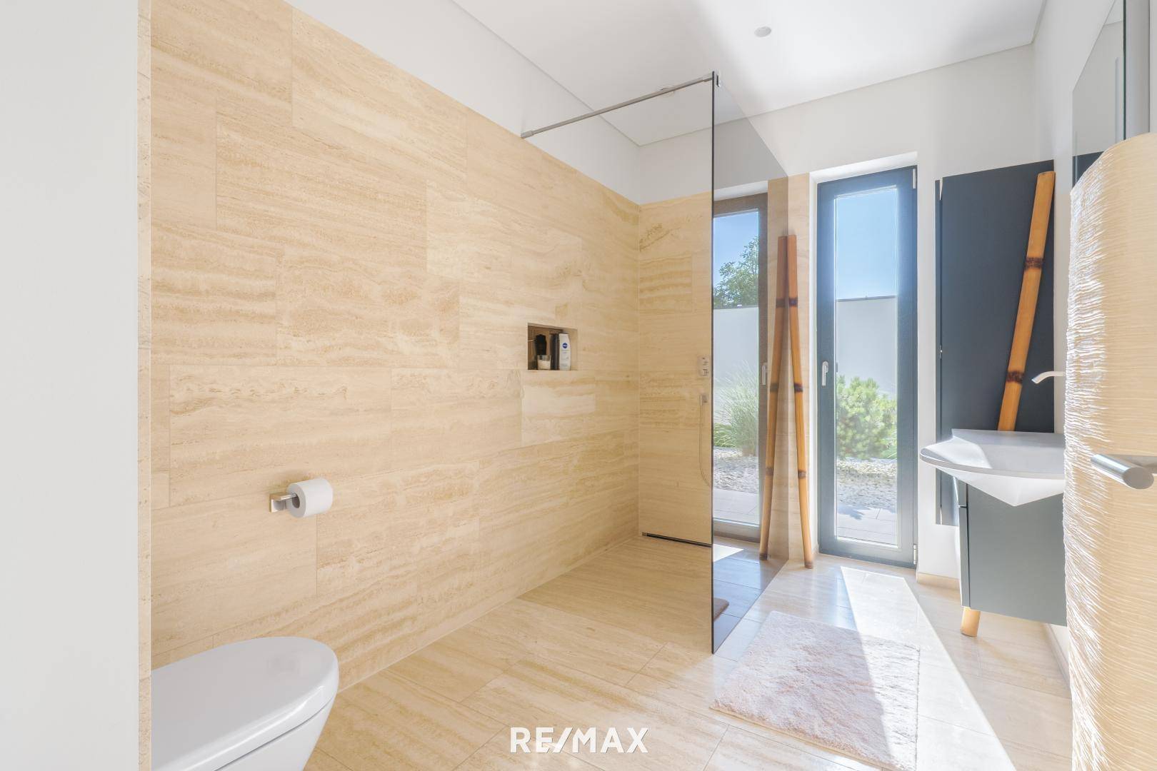 Modernes Badezimmer mit beigefarbenen Fliesen, ebenerdiger Dusche und großem Fenster für viel Tageslicht.