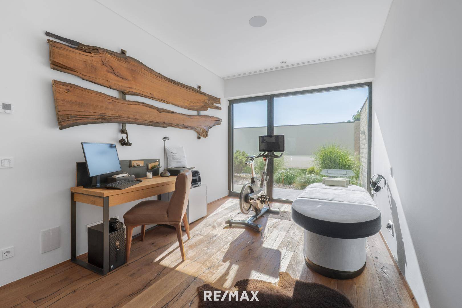 Helles Arbeitszimmer mit Holzboden, großem Fenster und Blick auf den Garten, ausgestattet mit Schreibtisch und Sportgerät.