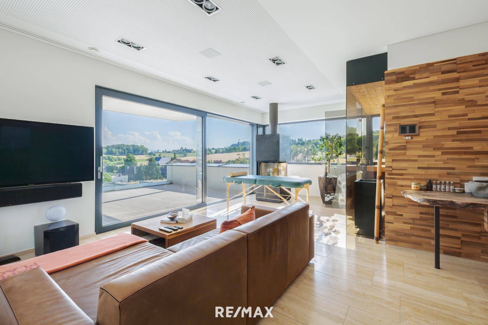 Modernes Wohnzimmer mit Kamin, Ledersofa und großen Fenstern, die einen weiten Blick über die Landschaft bieten.