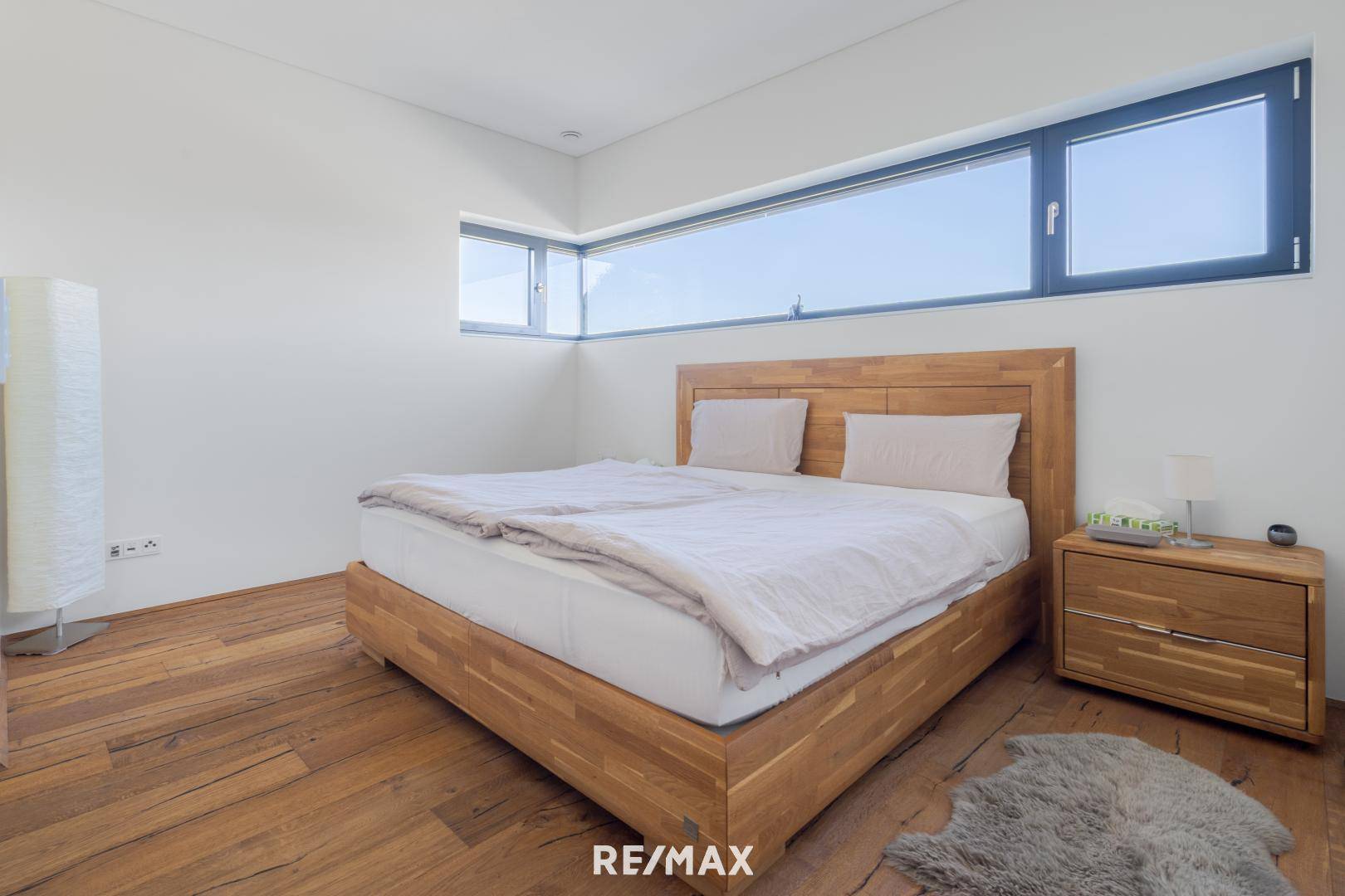 Gemütliches Schlafzimmer mit Holzbett, Holzboden und langen Fenstern, die viel Tageslicht hereinlassen.