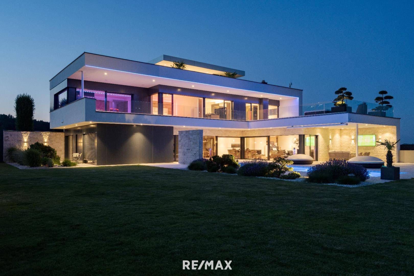 Elegante Villa bei Dämmerung mit beleuchtetem Poolbereich und stimmungsvoller Außenbeleuchtung.