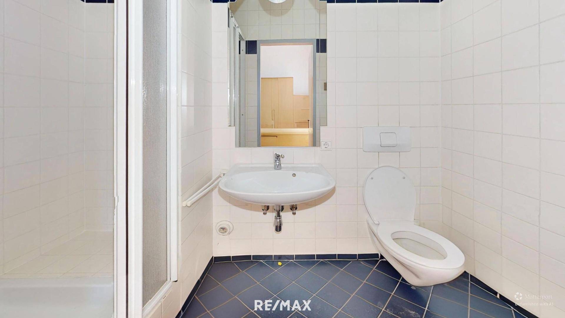 Einfaches Badezimmer mit Dusche, WC und Waschbecken, komplett gefliest in Weiß und Dunkelblau.