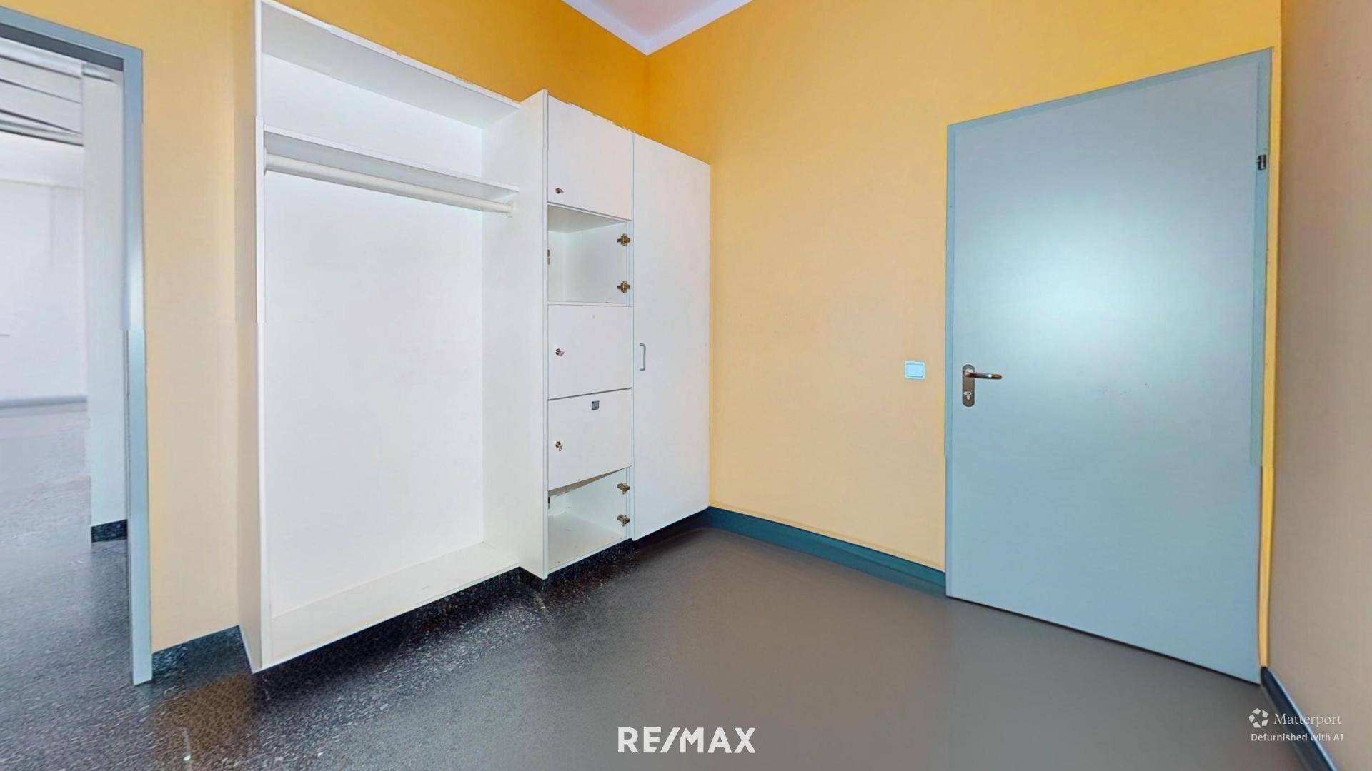 Kleiner Raum mit gelben Wänden, einem weißen Einbauschrank und dunklem Boden.
