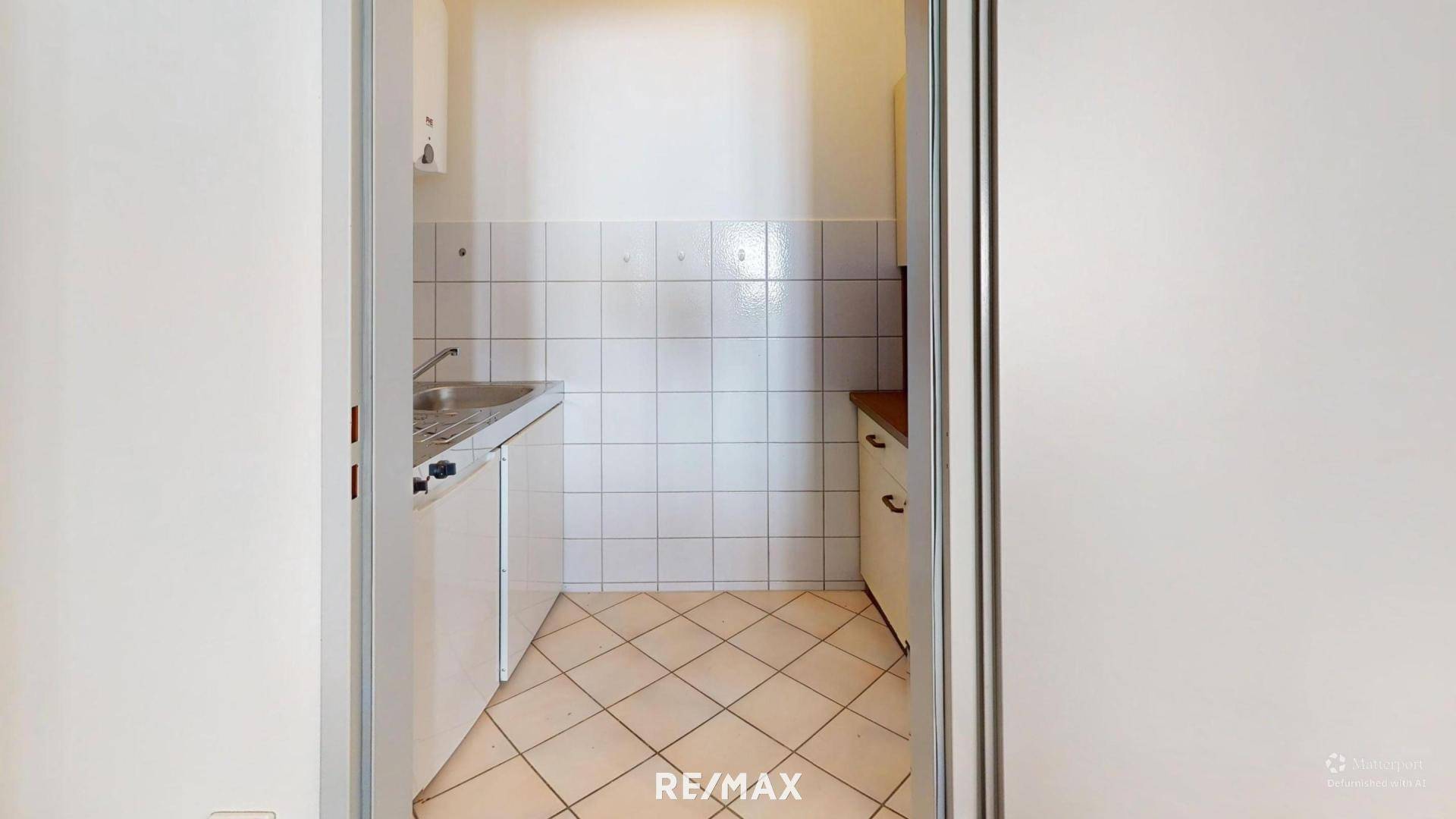 Kleine Küchenzeile mit weißen Fliesen, Spüle und Unterschränken, ideal für eine Büroküche.