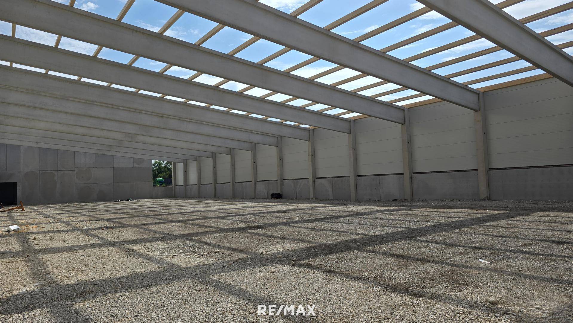 Im Bau befindliche Industriehalle mit offener Dachkonstruktion und Kiesboden, viel Tageslicht.