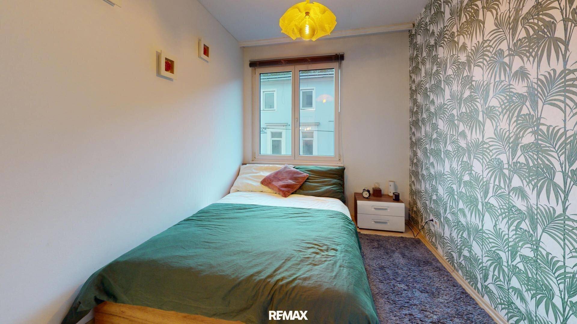 Kleines Schlafzimmer mit Einzelbett, Nachttisch und auffälliger Tapete mit Pflanzenmuster.