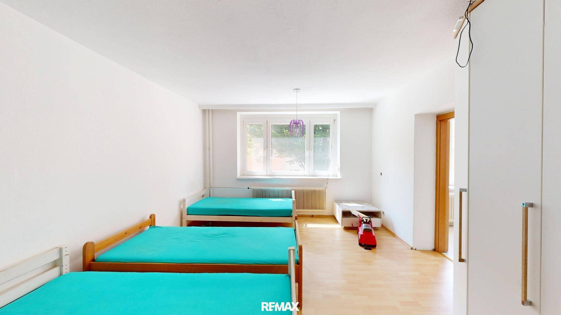 Helles Schlafzimmer mit mehreren Betten, Holzfußboden und großem Fenster.