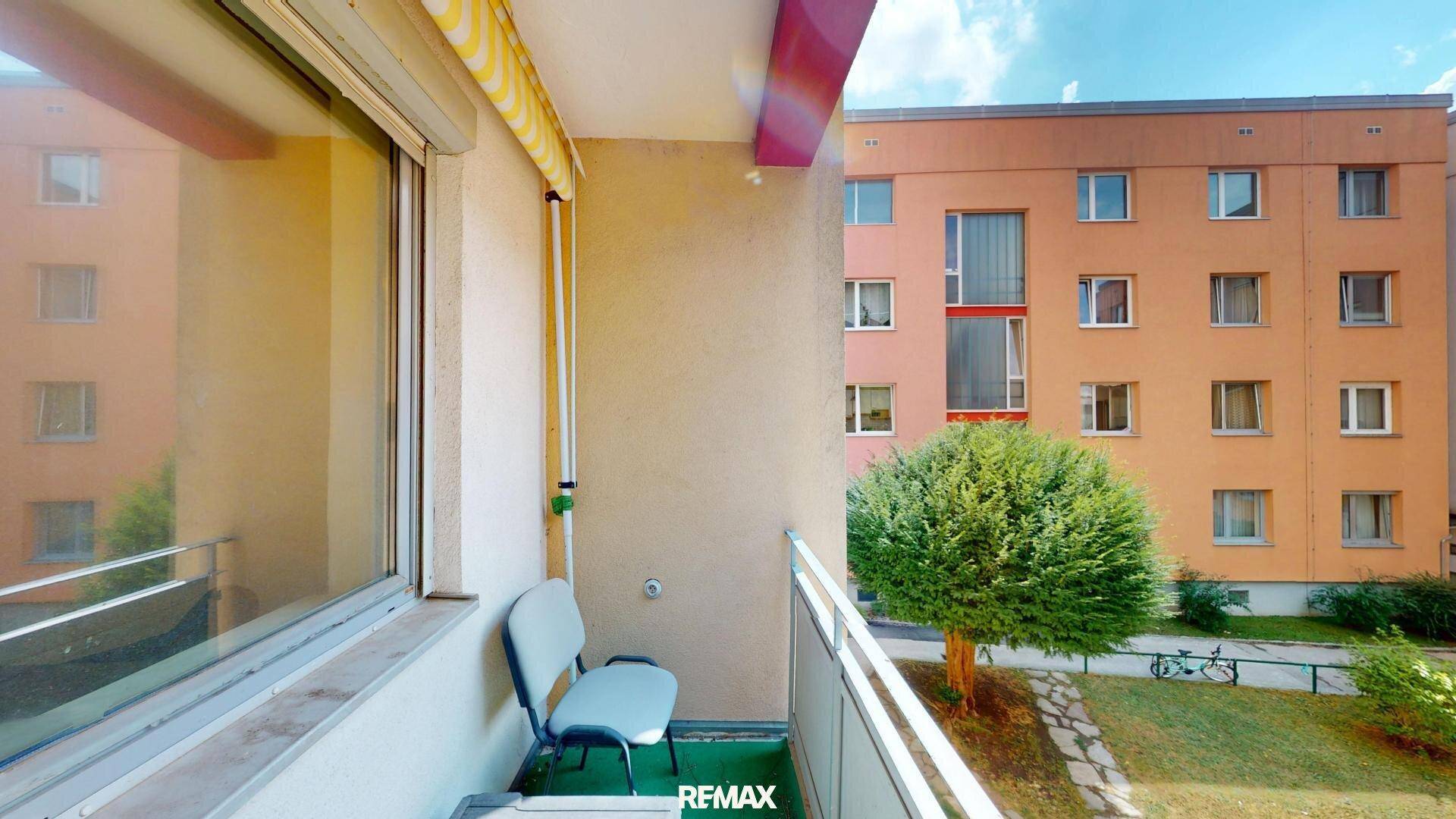 Kleiner Balkon mit Sitzgelegenheit und Blick auf den Innenhof und die umliegenden Gebäude.