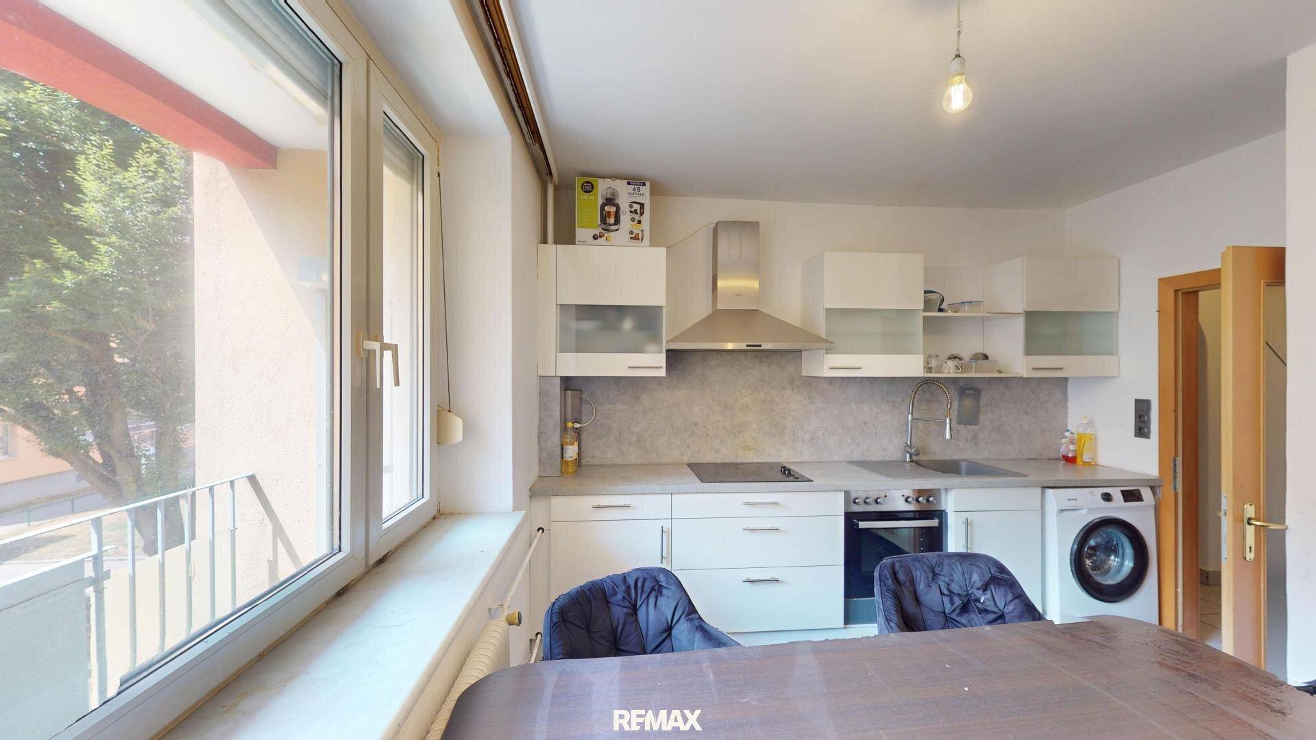 Funktionale Küche mit weißen Schränken, modernen Geräten und Zugang zum Balkon.
