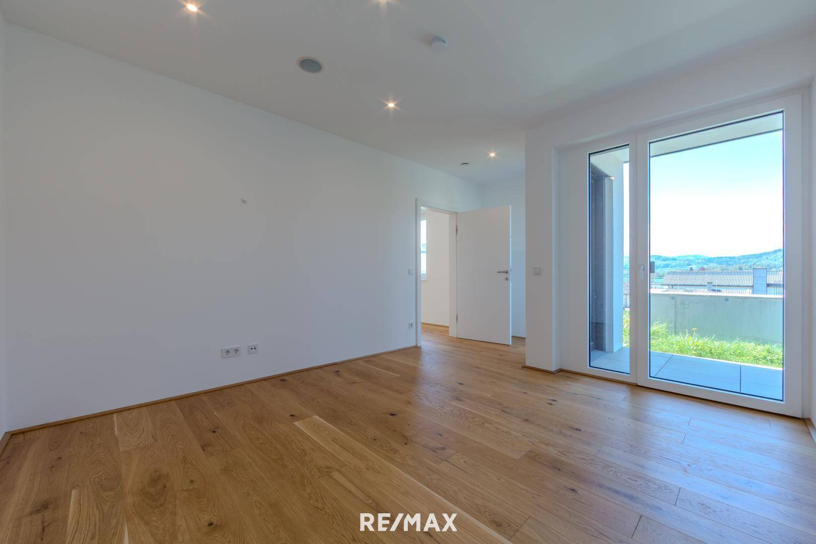 Helles Schlafzimmer mit Holzboden und Zugang zu einem Balkon mit Weitblick auf die Landschaft.
