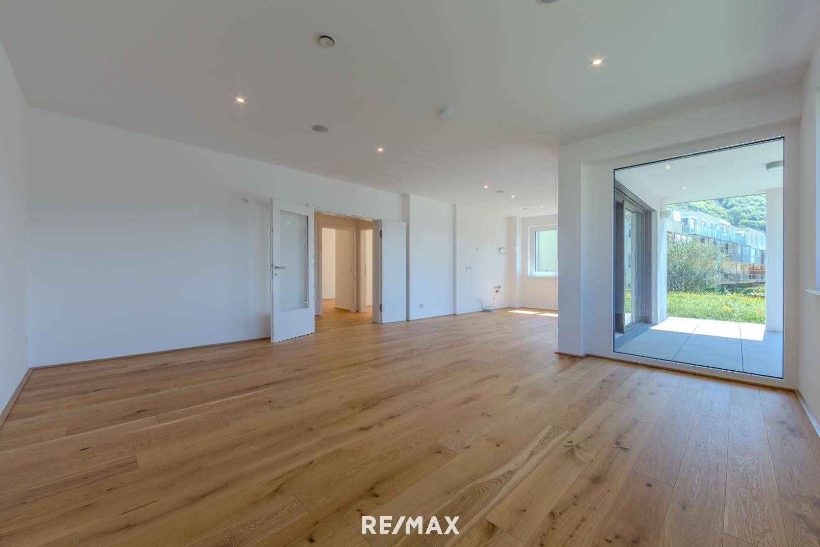Geräumiger, offener Wohnbereich mit Holzboden und viel Tageslicht durch große Fenster und Terrassenzugang.