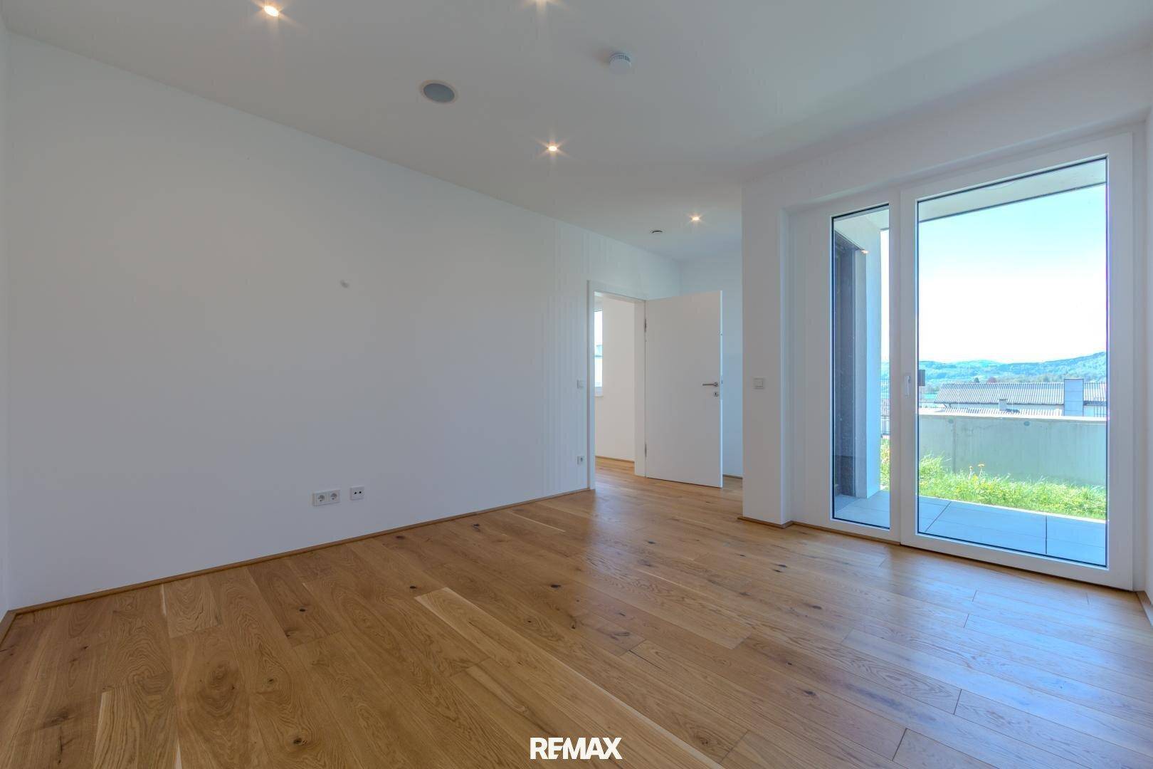 Geräumiger, heller Raum mit Holzboden und Zugang zu einem Balkon mit Weitblick.