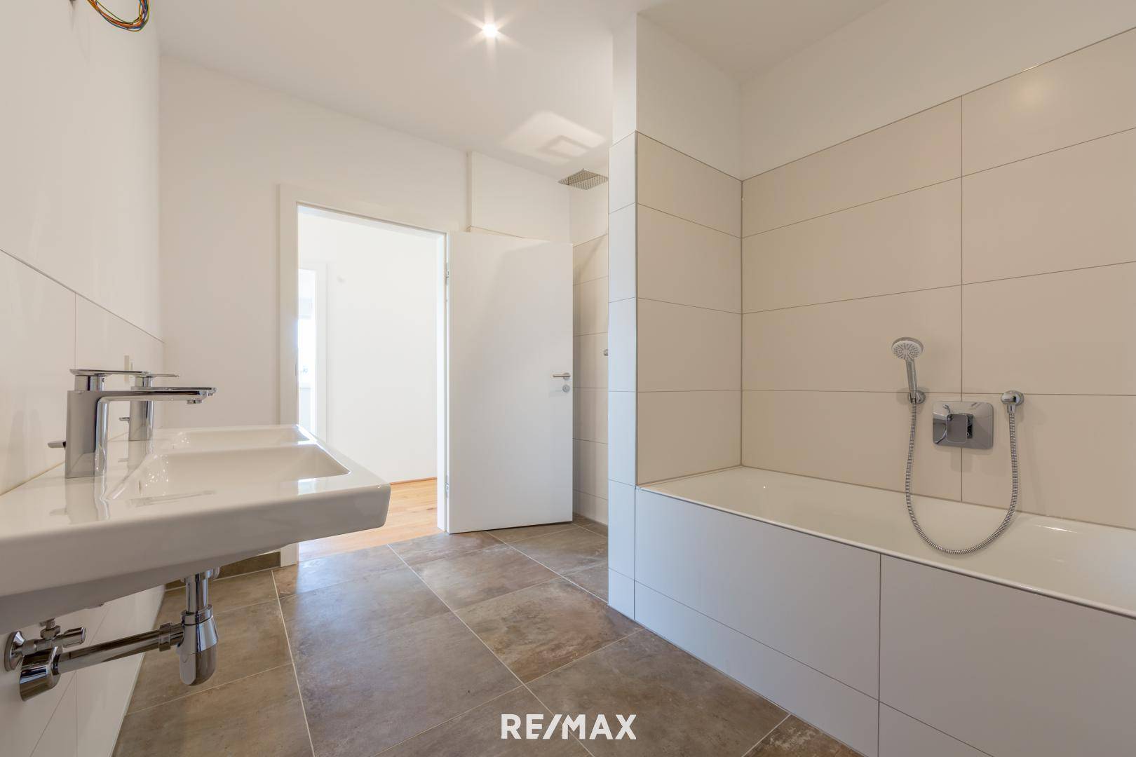 Modernes Badezimmer mit Doppelwaschbecken, Badewanne und hellen Fliesen an Wänden und Boden.