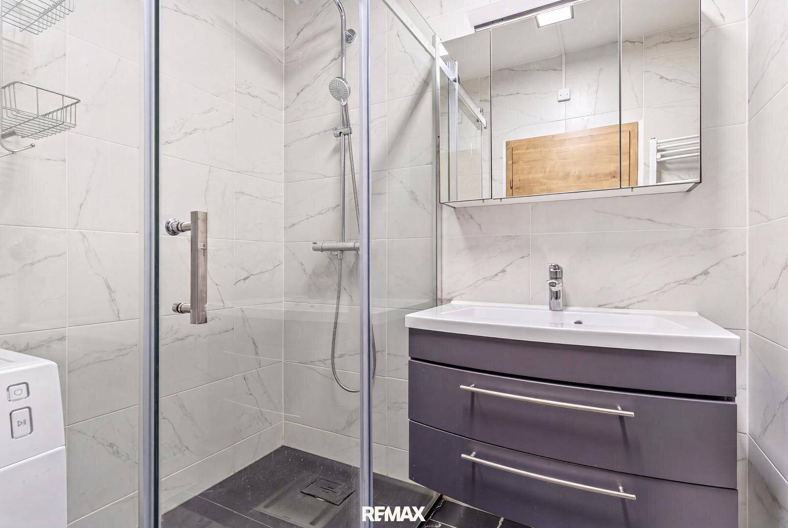 Modernes Badezimmer mit Duschkabine, Waschbecken und Spiegelschrank.