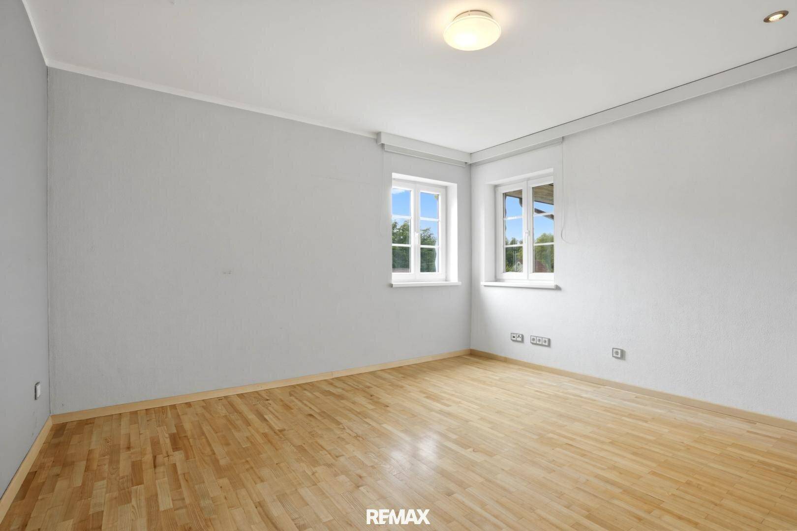 Helles Schlafzimmer mit Parkettboden und zwei Fenstern, die viel Tageslicht hereinlassen.