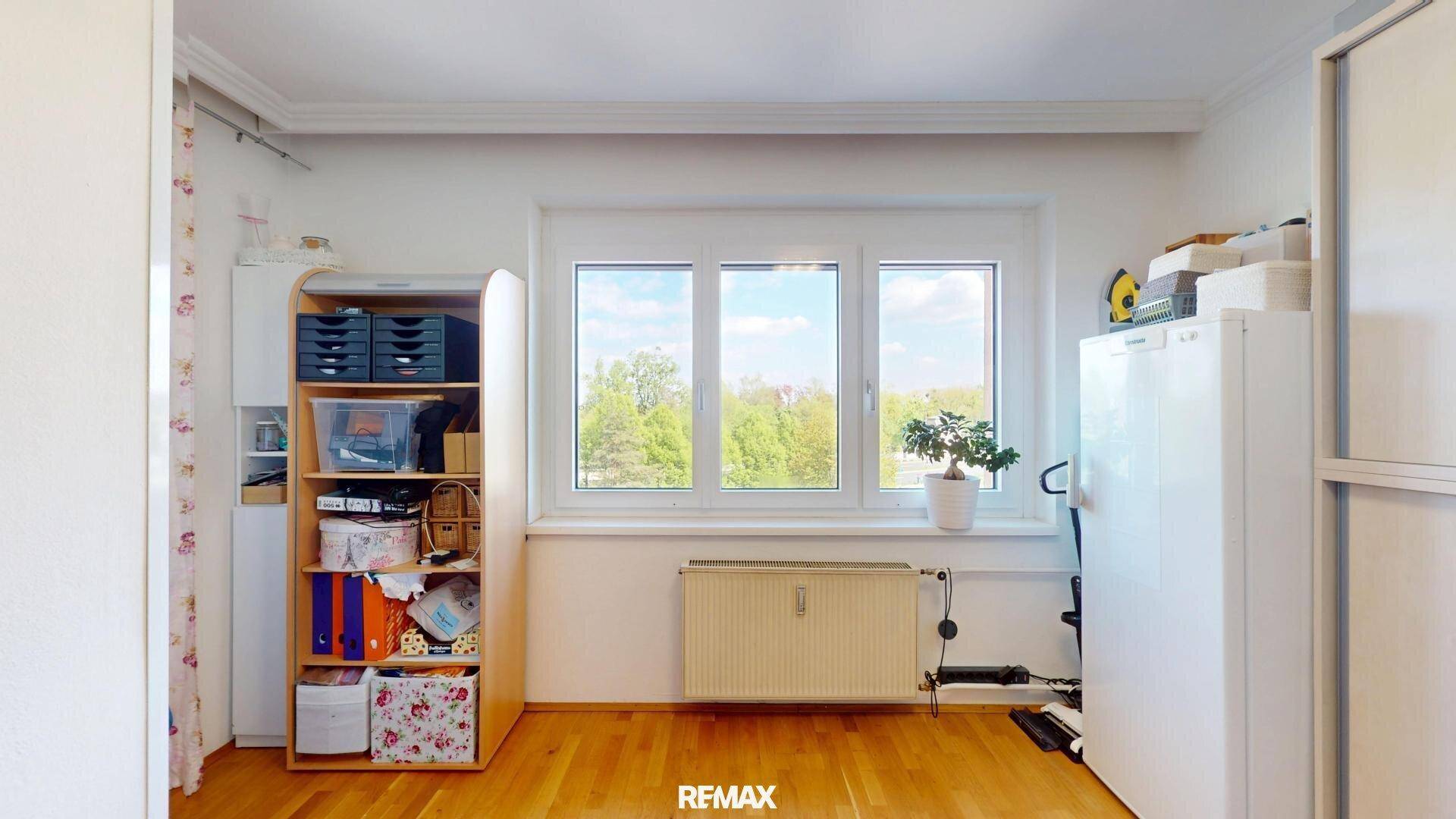 Geräumiges Arbeitszimmer mit Blick ins Grüne, ausgestattet mit Regalen und einem Heizkörper unter dem Fenster.